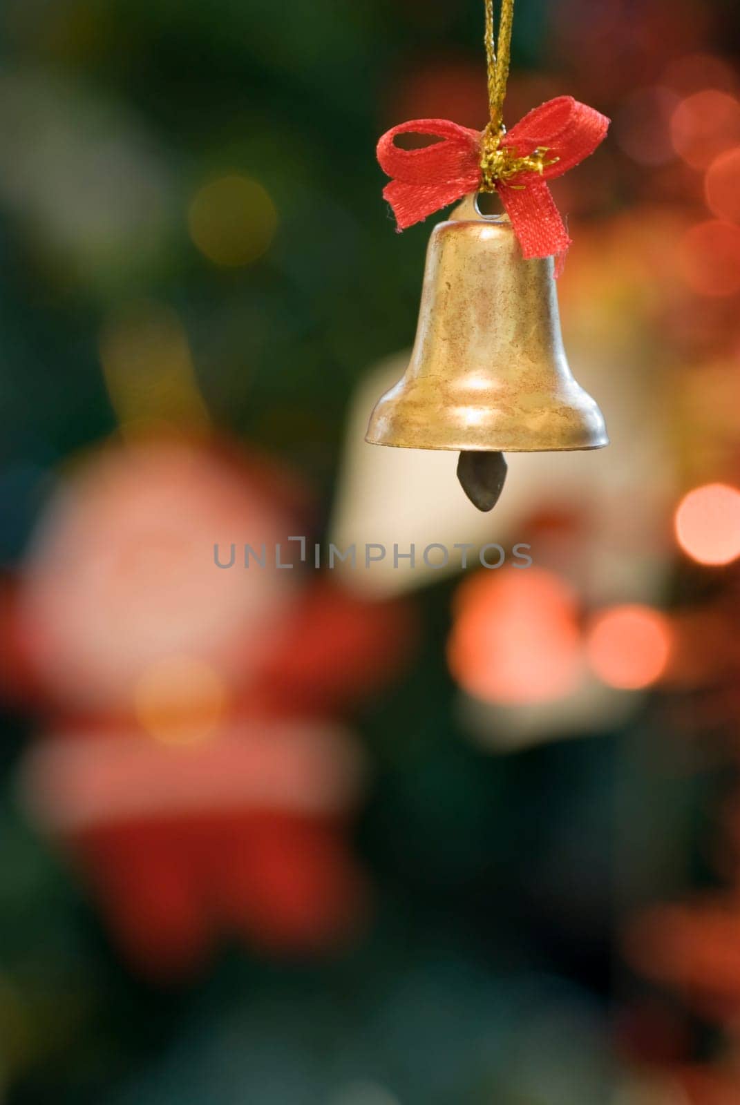 Decorative xmas bell with red ribbon with blurred xmas tree decoration in the background.