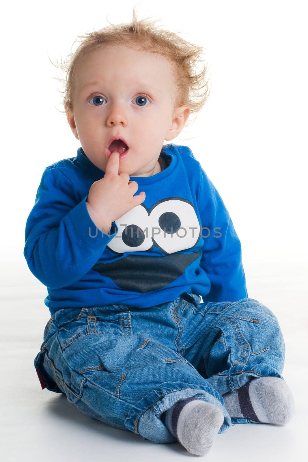 Happy cute baby sitting on white with finger in mouth