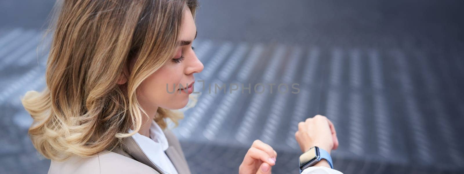 Close up portrait of business woman looking at her wrist digital watch, reading message, using app, standing outdoors in city center.