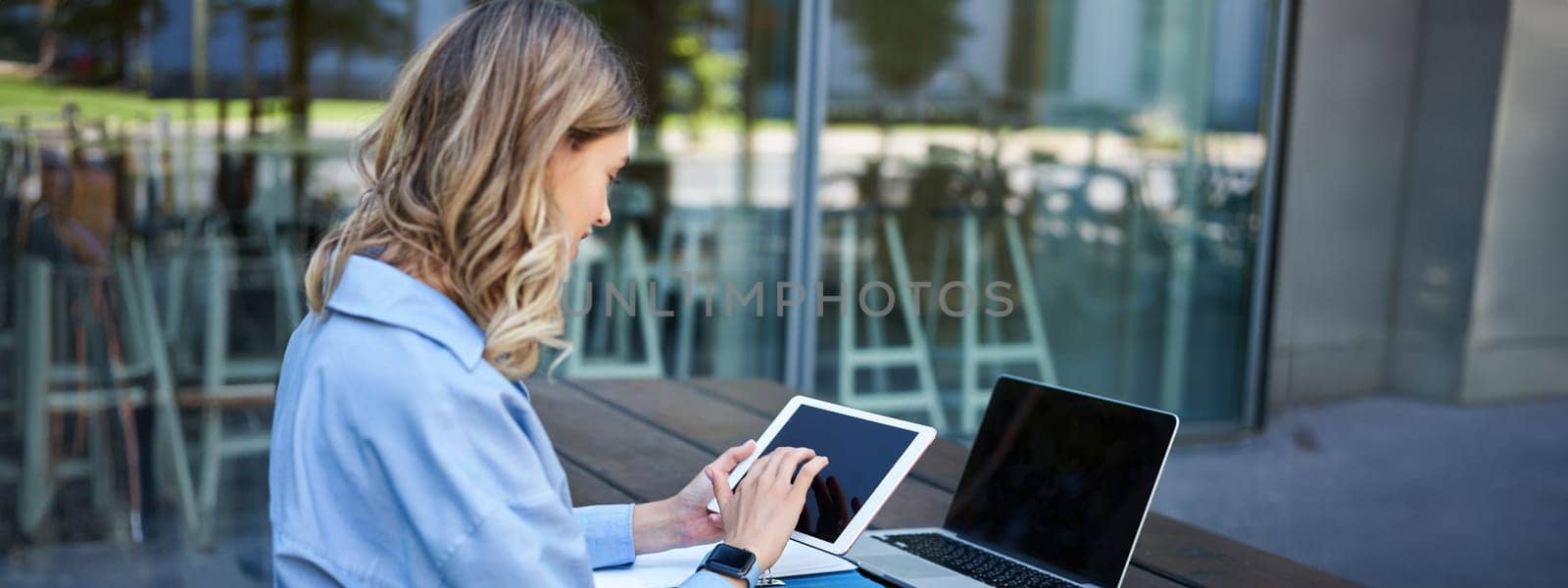 Portrait of businesswoman working on digital tablet, checking diagrams, sitting outdoors on fresh air near office building. Corporate woman prepare for work meeting by Benzoix