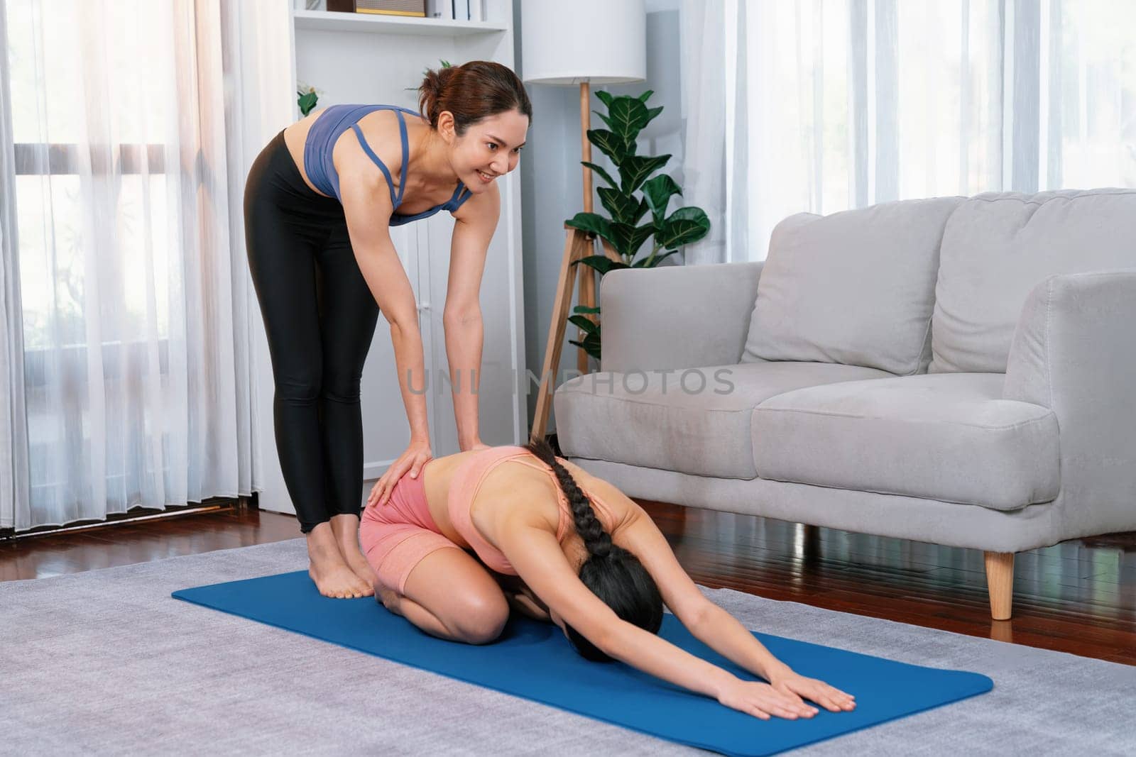 Asian woman doing yoga exercise on fitness mat with trainer. Vigorous by biancoblue