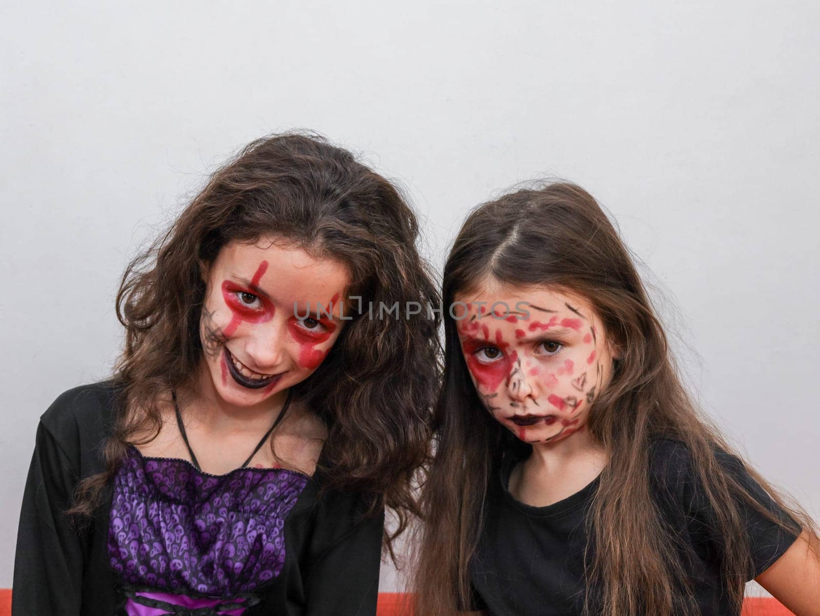 Portrait of two girls sisters in a witch costume with colorful Halloween makeup. by Nataliya