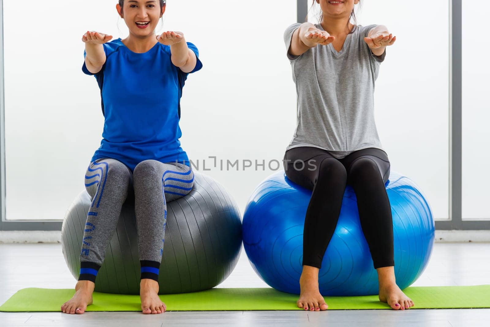 adult and young woman in sportswear doing aerobics yoga exercise with sitting on fitness ball by Sorapop
