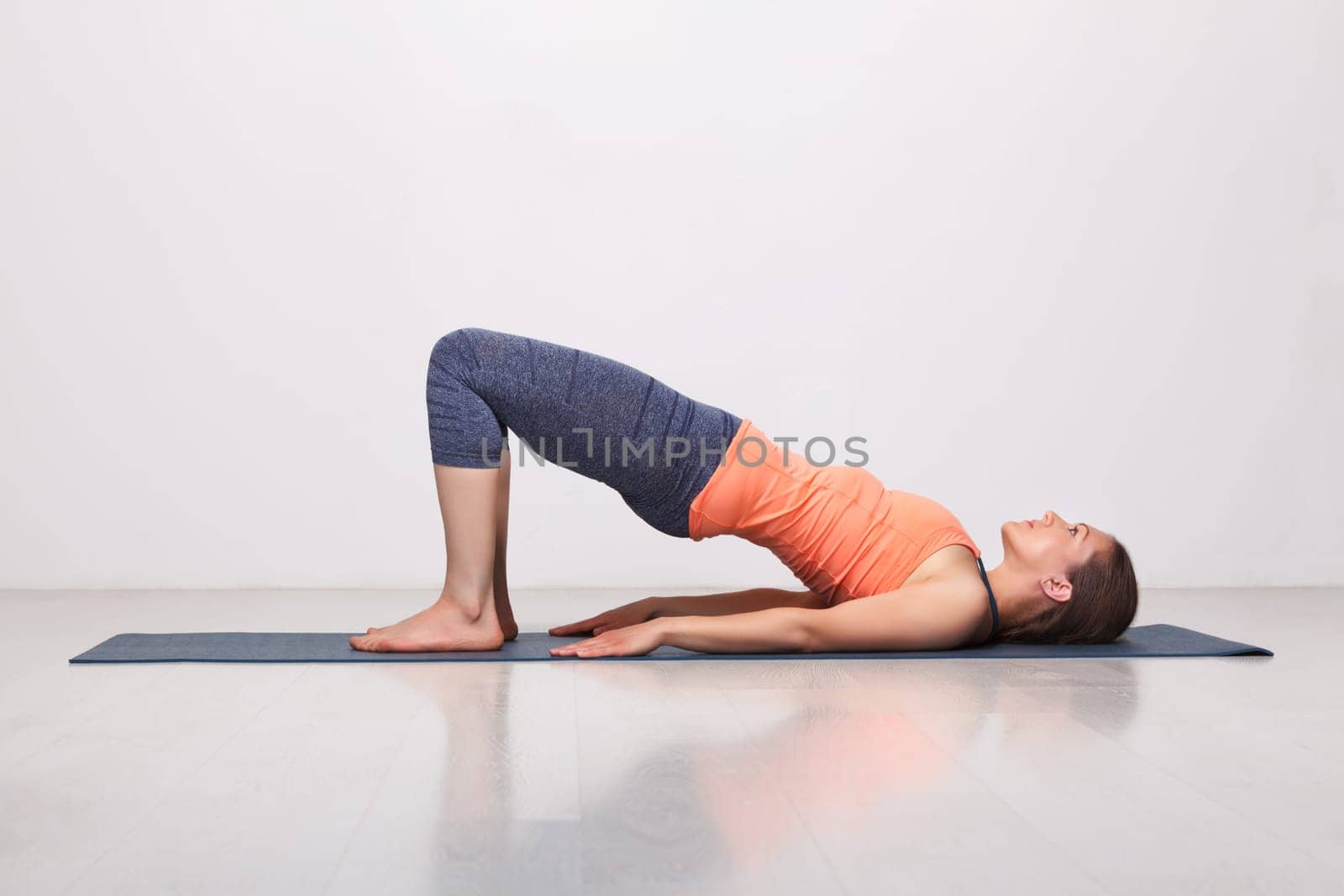 Beautiful sporty fit yogini woman practices yoga asana setu bandhasana - bridge pose beginner variation in studio