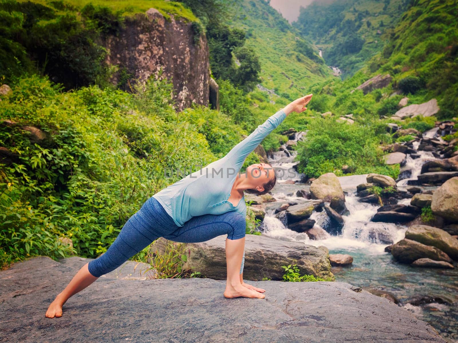 Vintage retro effect hipster style image of fit woman practices yoga asana Utthita Parsvakonasana - extended side angle pose outdoors at water