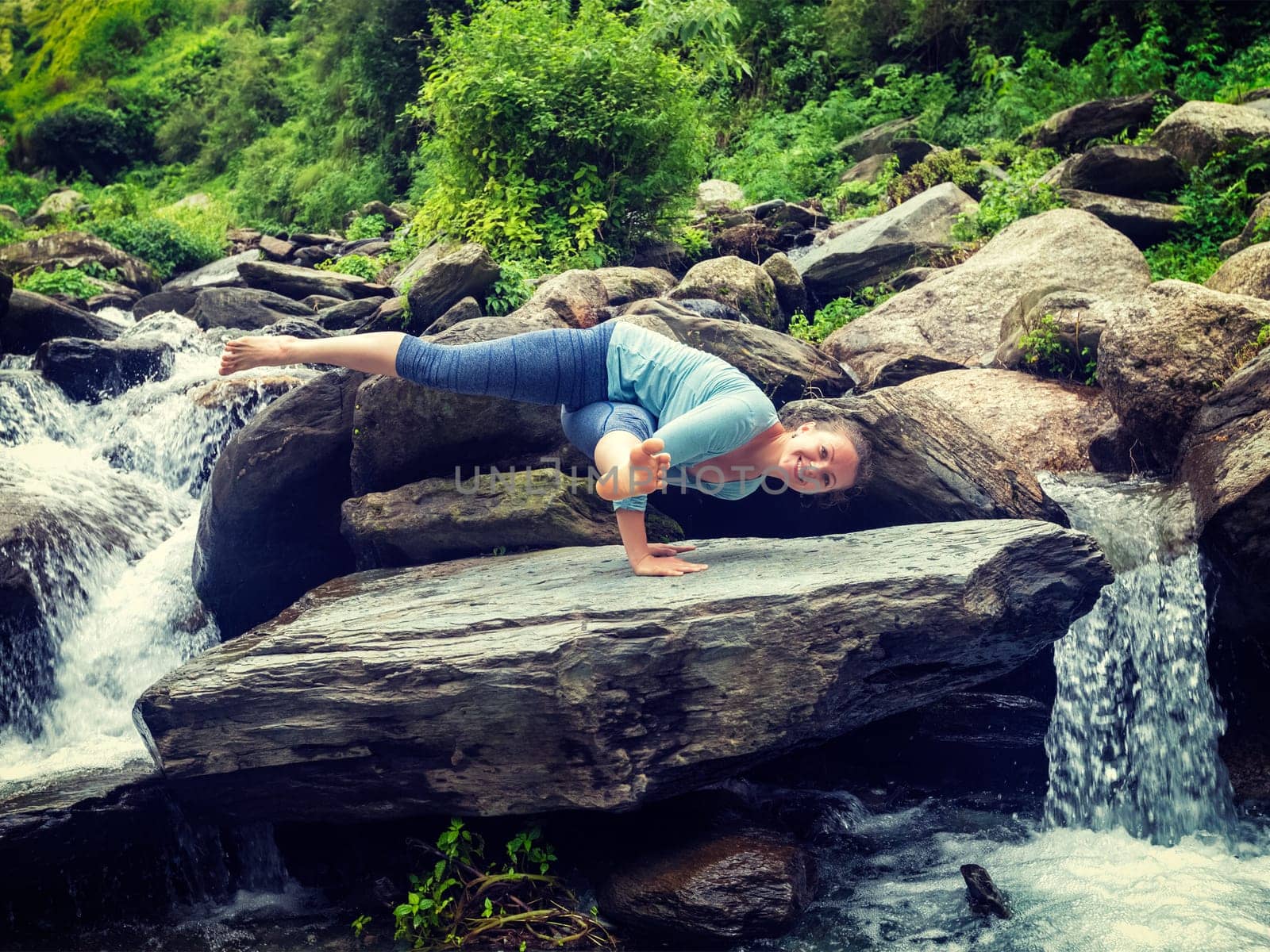 Young sporty fit woman doing yoga oudoors at tropical waterfall by dimol