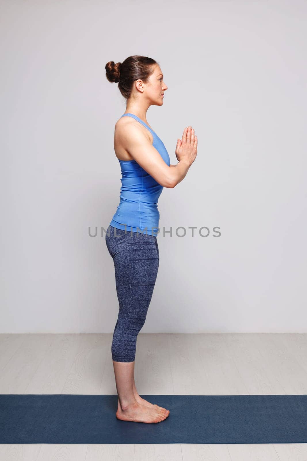 Woman doing Hatha Yoga asana Tadasana namaste -Mountain pose with salutation on yoga mat in studio on grey bagckground