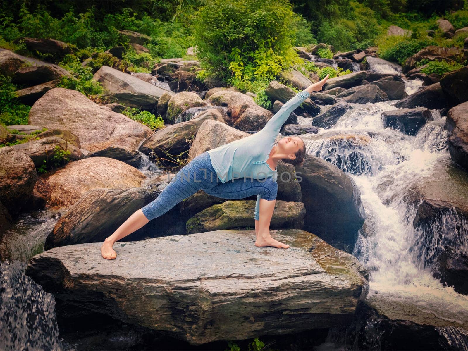 Vintage retro effect hipster style image of fit woman practices yoga asana Utthita Parsvakonasana - extended side angle pose outdoors at water
