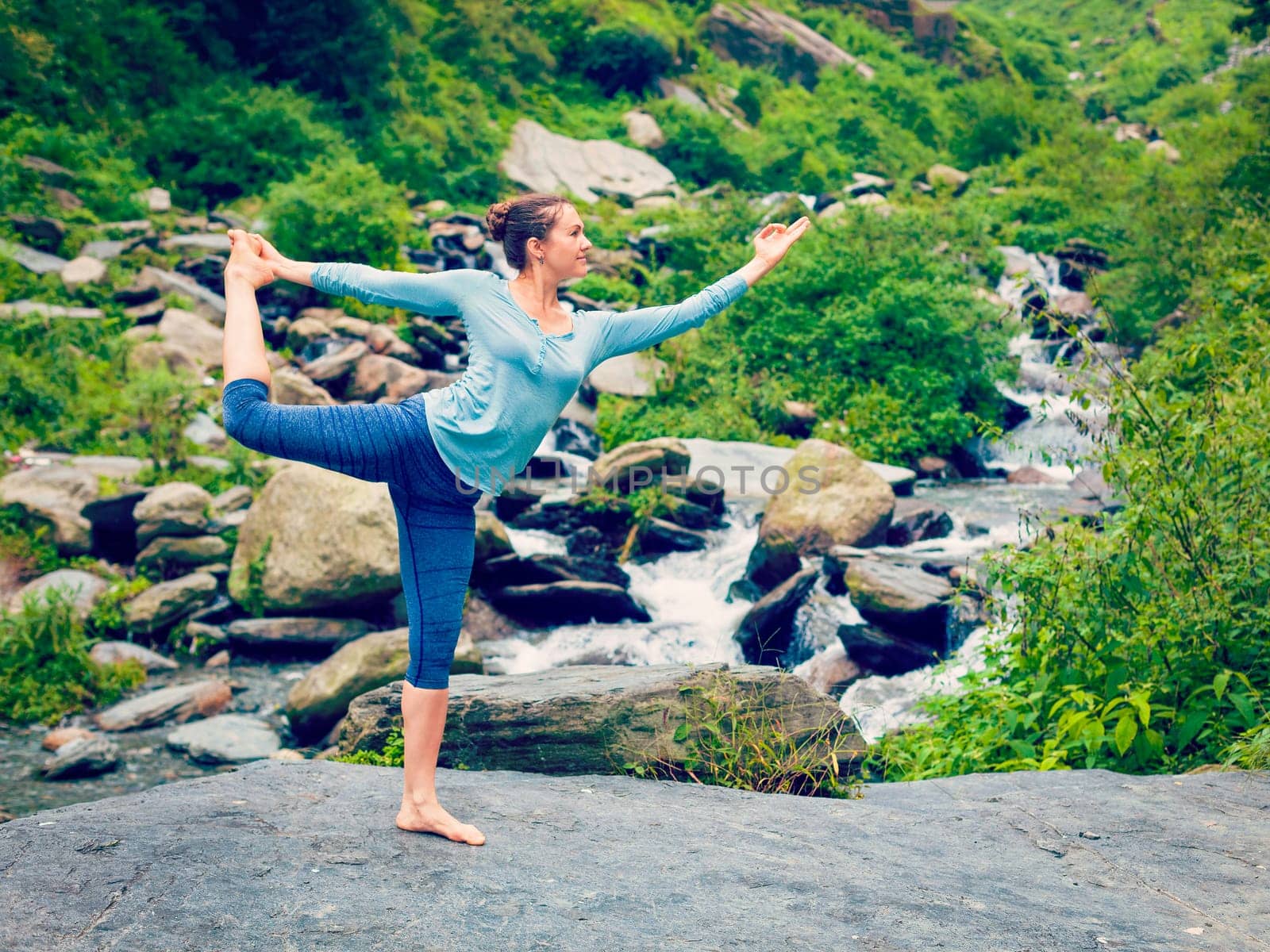 Vintage retro effect hipster style image of woman doing yoga asana Natarajasana - Lord of the dance pose outdoors at waterfall in Himalayas
