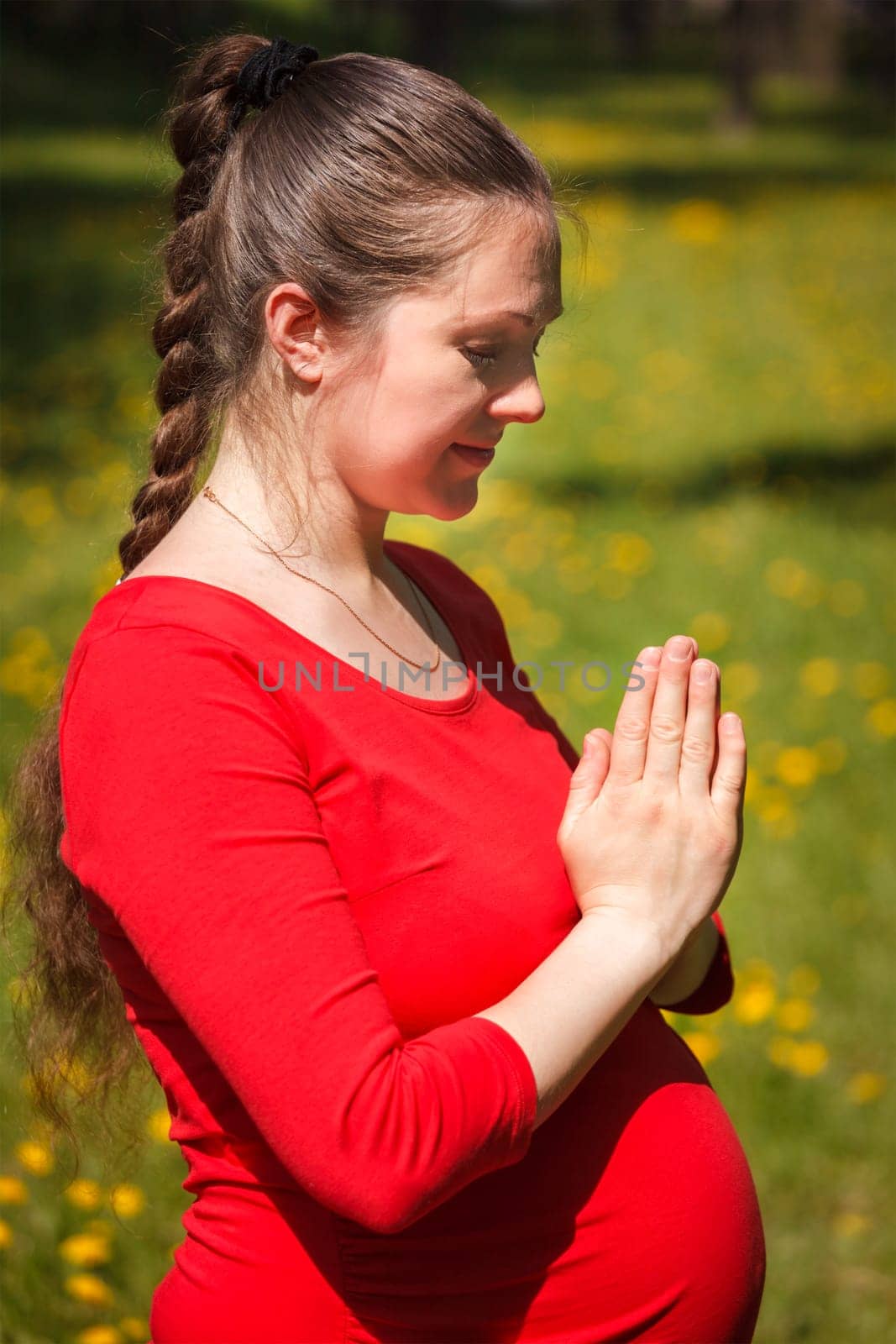 Pregnancy yoga exercise - pregnant woman doing asana Tadasana namaste -Mountain pose with salutation outdoors on grass lawn with dandelions in summer