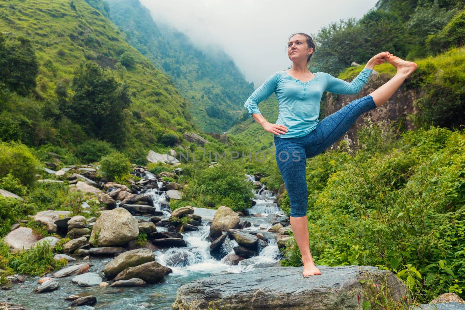 Yoga outdoors - woman doing Ashtanga Vinyasa Yoga balance asana Utthita Hasta Padangushthasana - Extended Hand-To-Big-Toe Pose position posture outdoors at waterfall