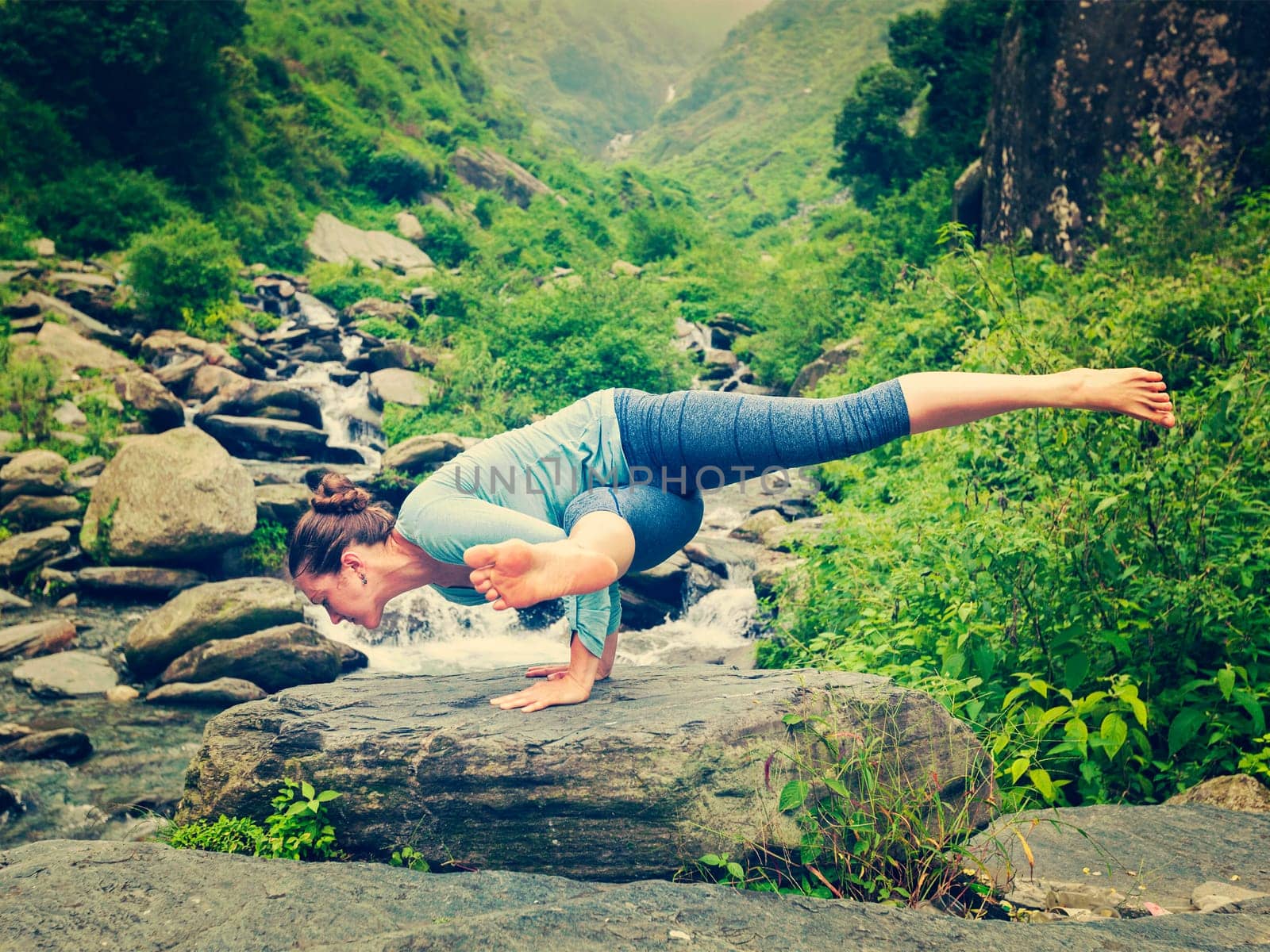 Young sporty fit woman doing yoga oudoors at tropical waterfall by dimol