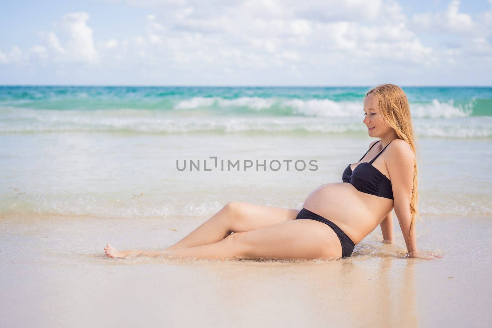 Radiant pregnant woman in a swimsuit, amid the stunning backdrop of a turquoise sea. Serene beauty of maternity by the shore.