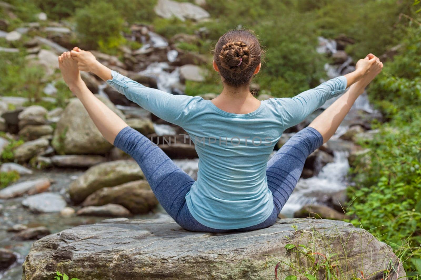 Woman doing Ashtanga Vinyasa Yoga asana Upavistha konasana outdoors at tropical waterfall