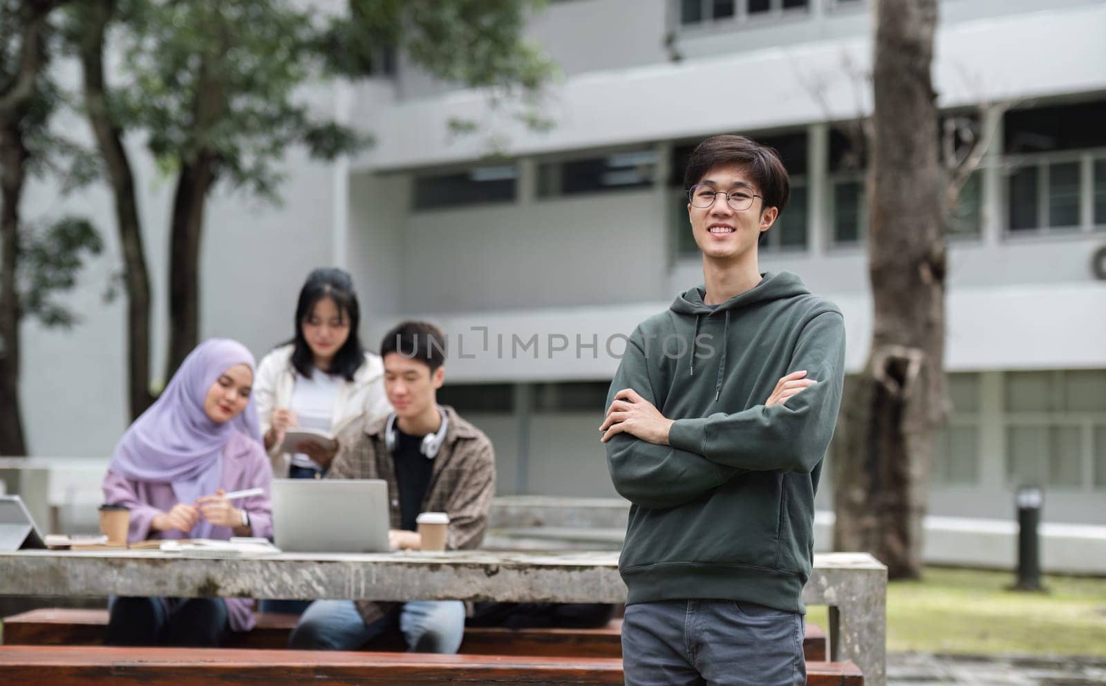 Portrait of Asian student studying in university garden. Young people spend time together, reading books, working on laptops, tablets. by wichayada