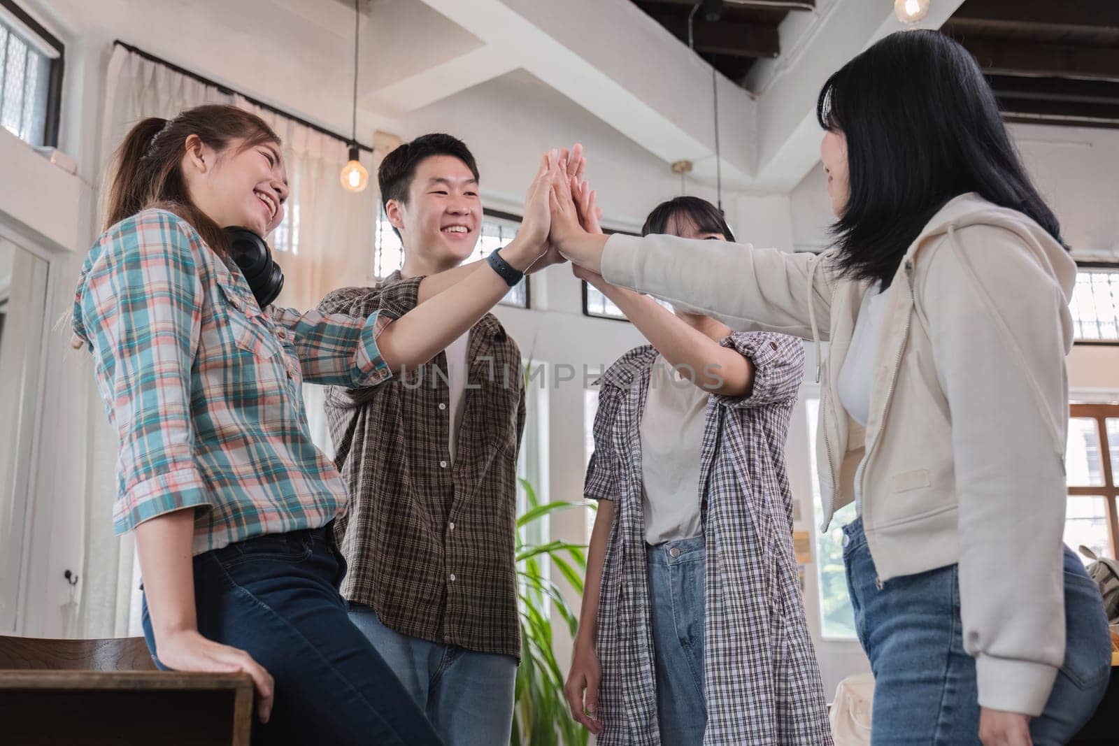 A group of cheerful and happy young Asian friends are gathering together to celebrate the success of a project together in a conference room. by wichayada