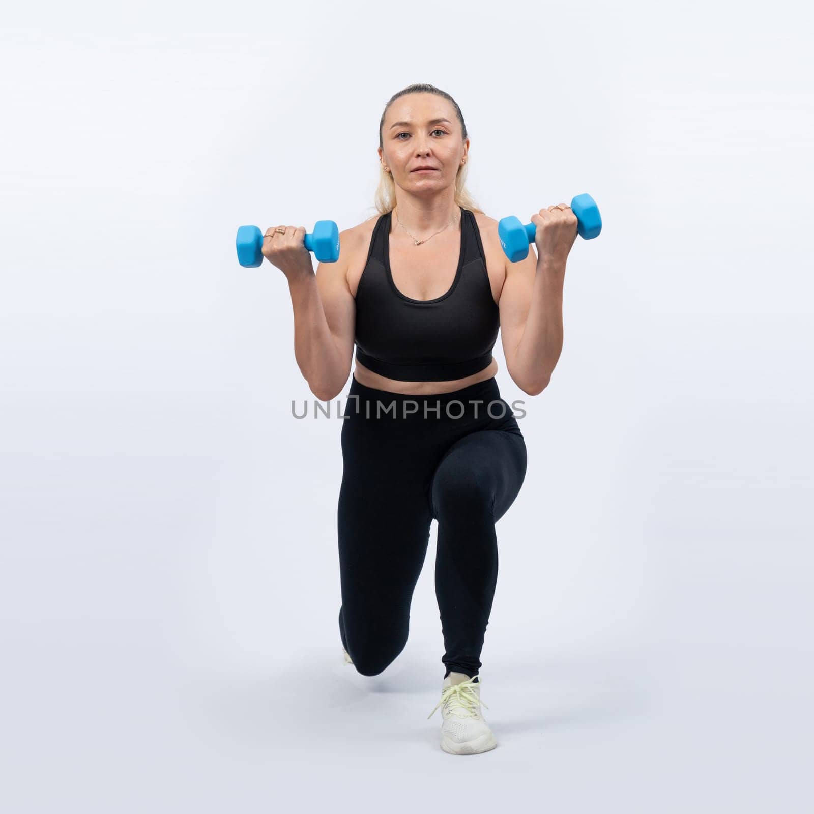 Full body length shot active and sporty senior woman lifting dumbbell during weight training workout on isolated background. Healthy active physique and body care lifestyle for pensioner. Clout