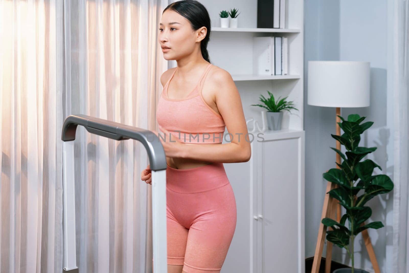 Energetic and strong athletic asian woman running running machine at home. Pursuit of fit physique and commitment to healthy lifestyle with home workout and training. Vigorous
