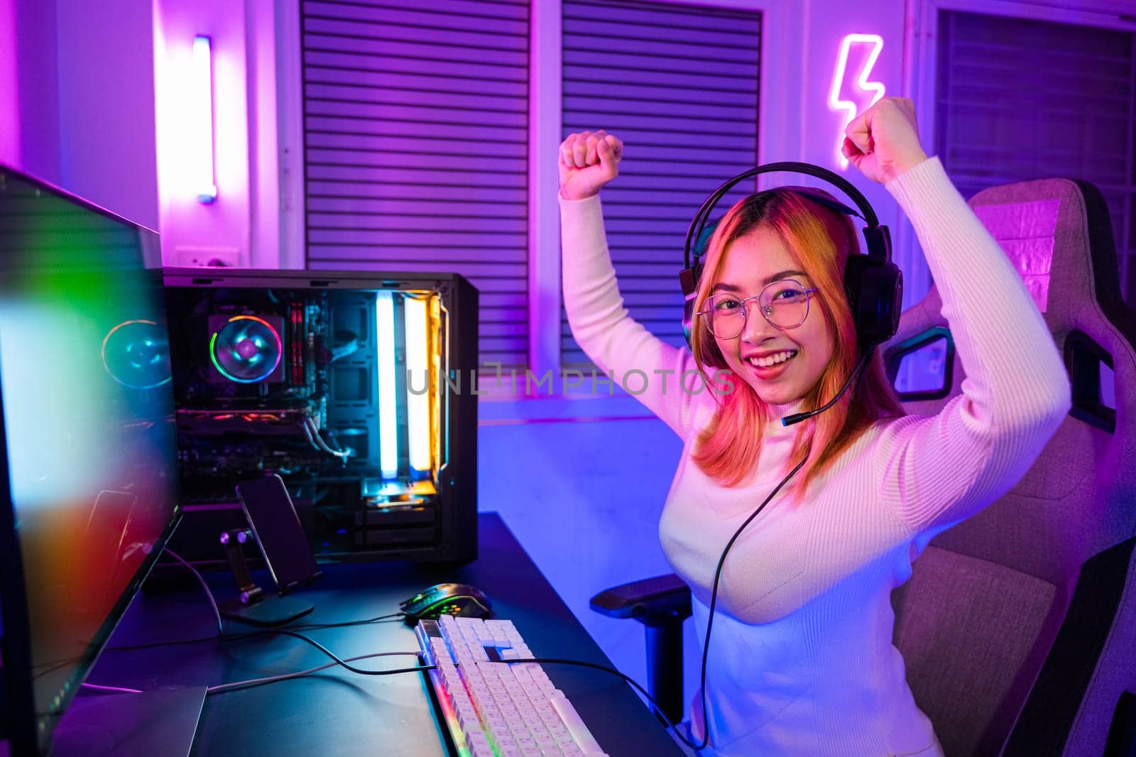 Winning. Happy Gamer young plays online video games computer she raises hands to wins tournament, young woman in gaming headphones playing video game online at home feel excited, E-Sport concept