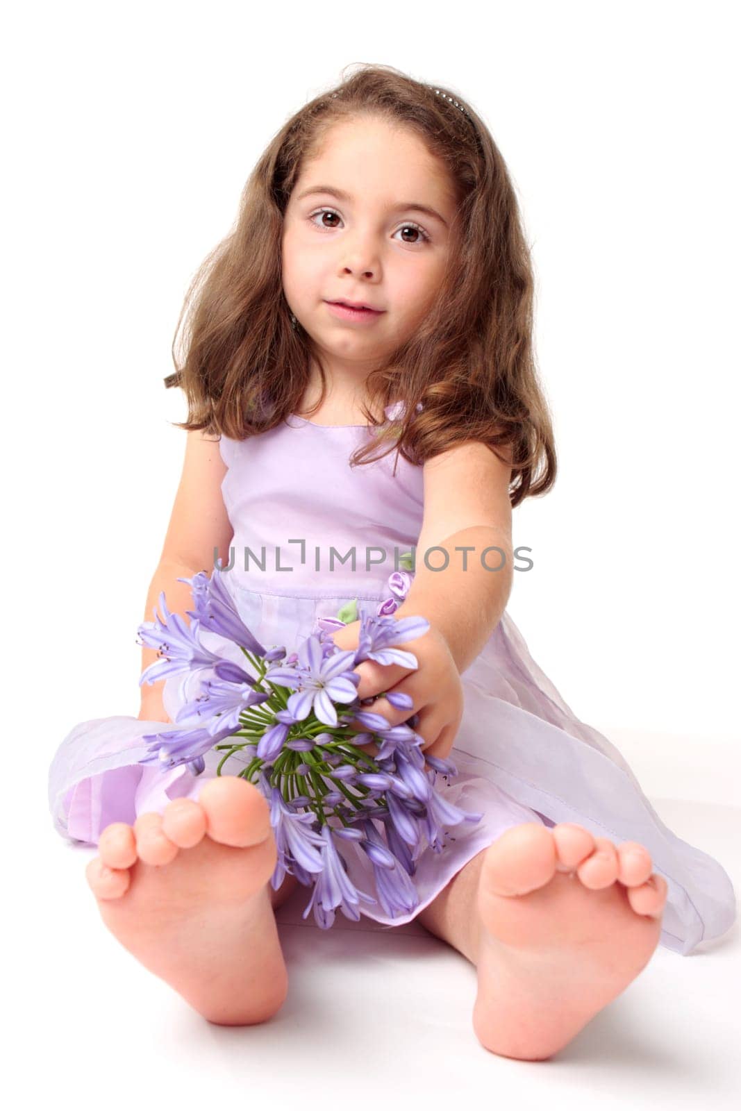 A young toddler girl wearing a pretty dress and sitting on the floor with a large agapanthus flower