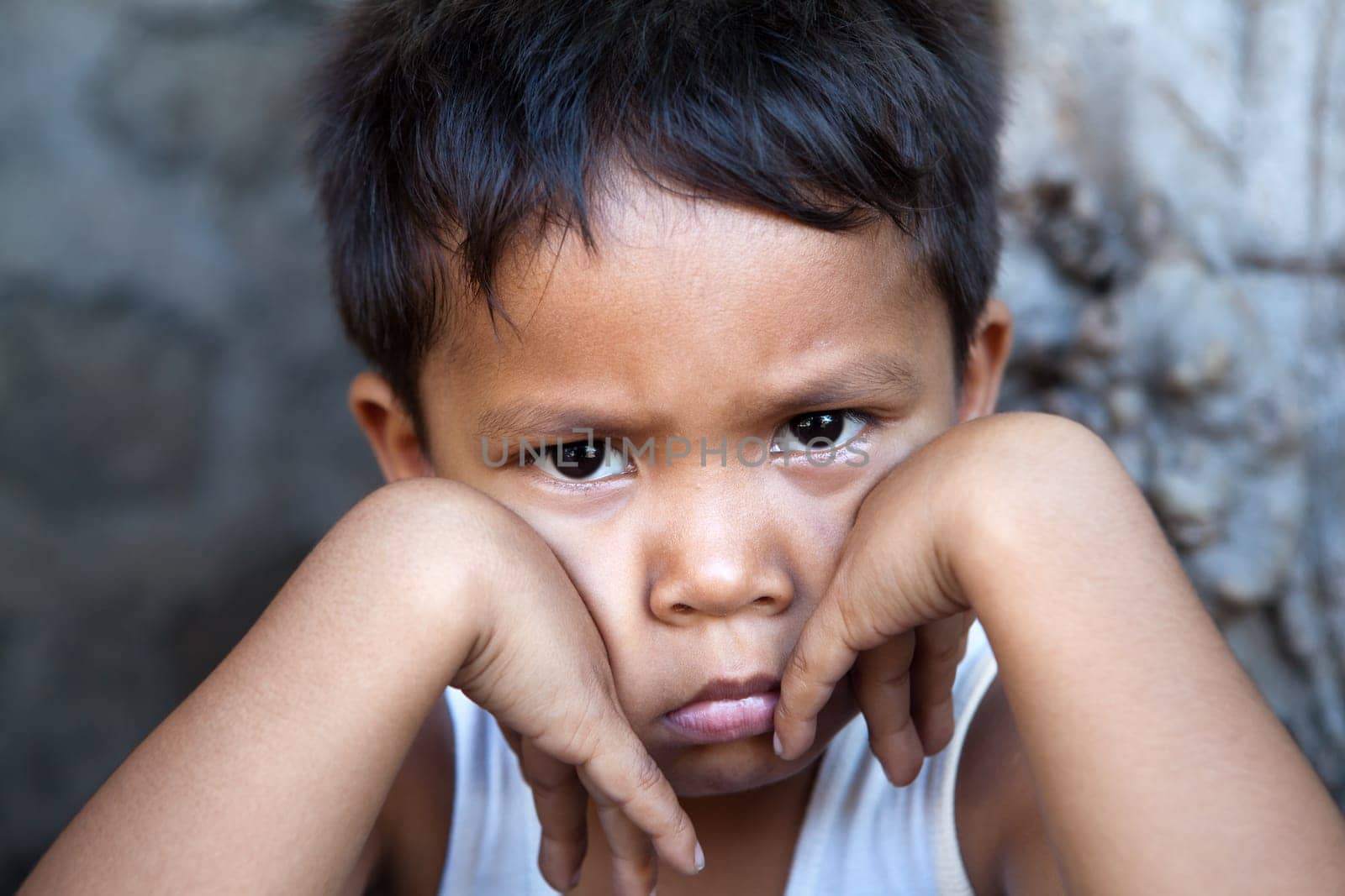 Young Filipino boy with sad expression against wall - poverty in the Philippines.