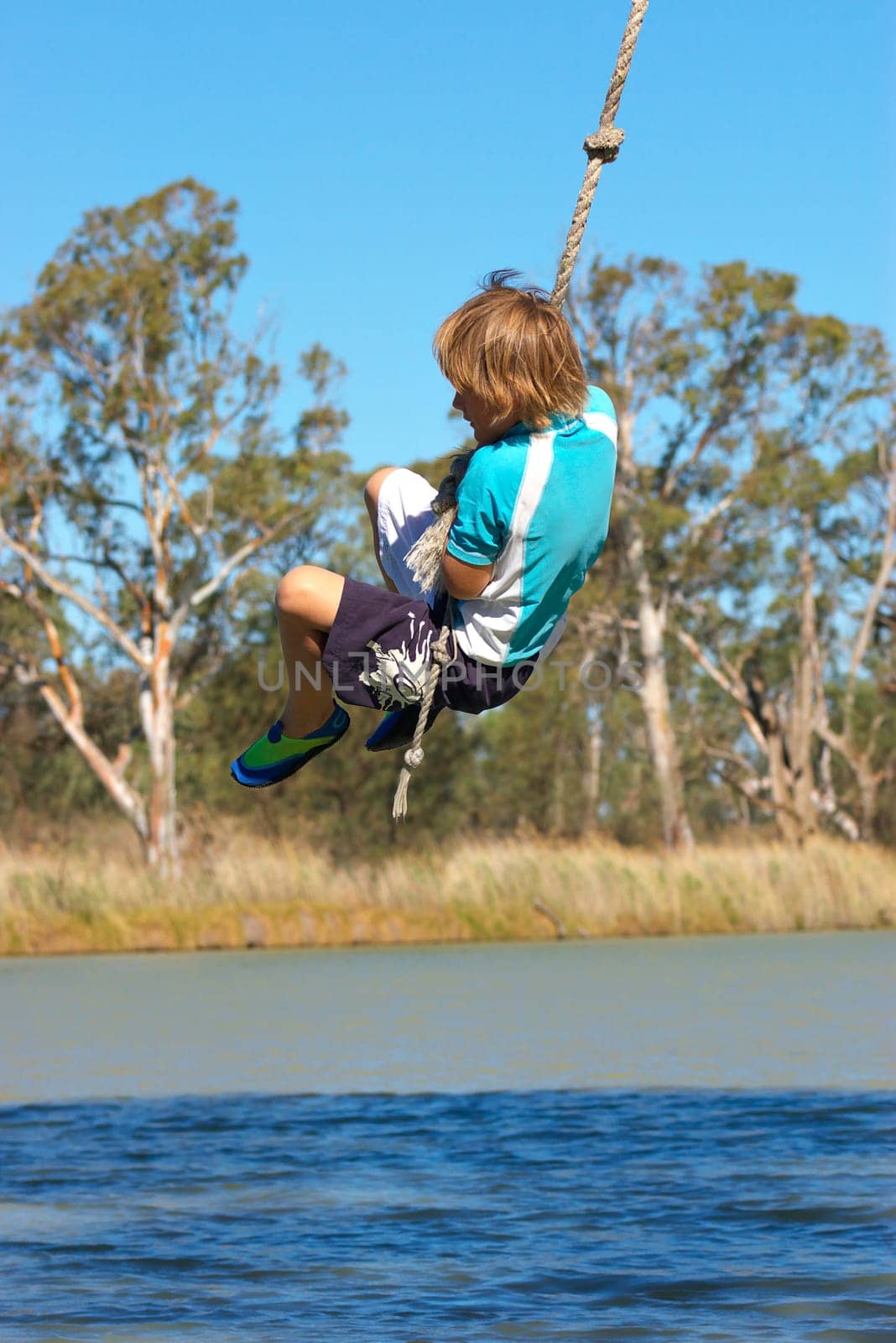 a boy is swinging on a rope over a river in summer