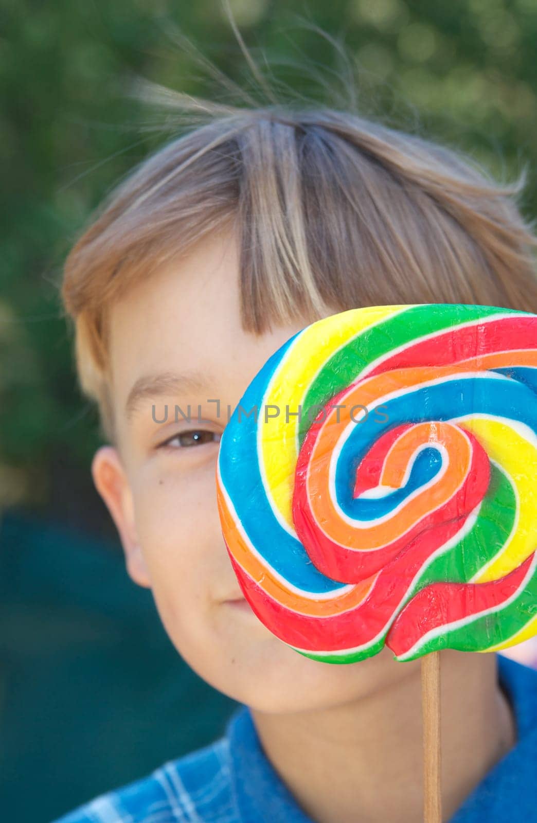 young boy looks around from behind a big swirly lollipop