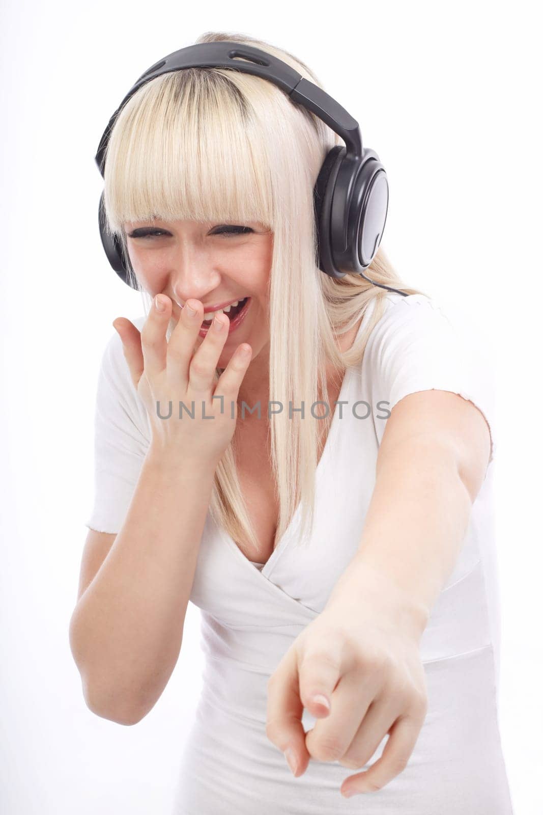 Portrait of laughing woman listening music and pointing down on an isolated white background