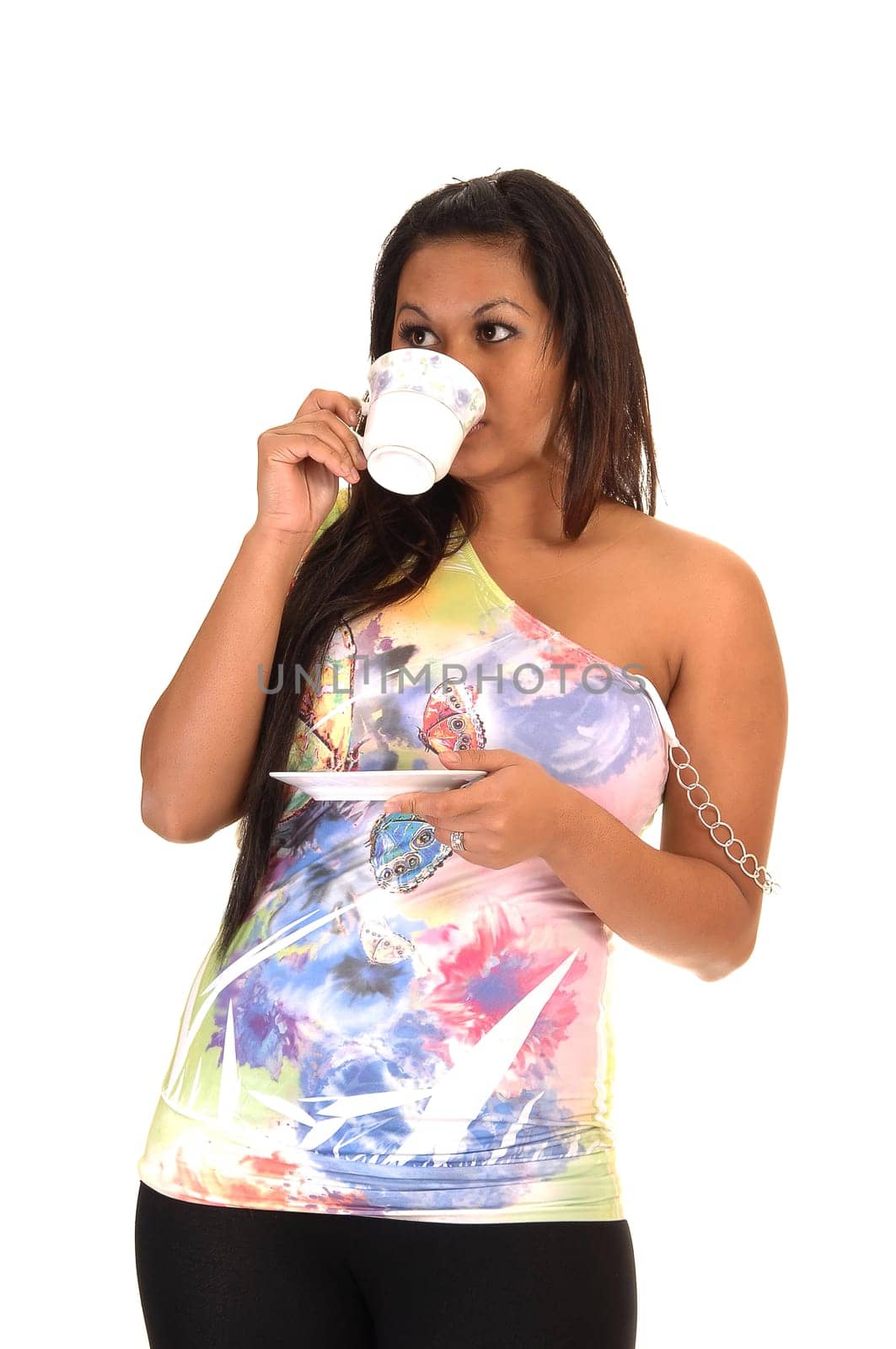 A pretty Asian woman drinking her coffee and holding the saucer, in a colorful blouse and long black hair, for white background.