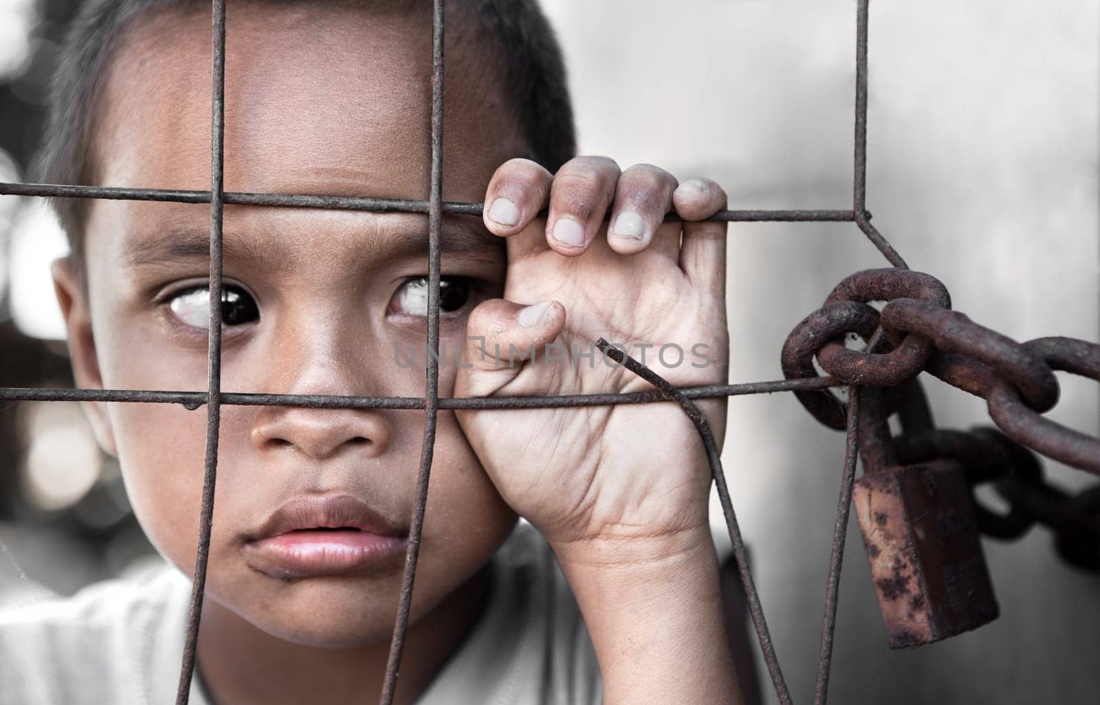 young Asian boy behind fence, slight grain, focus on hand