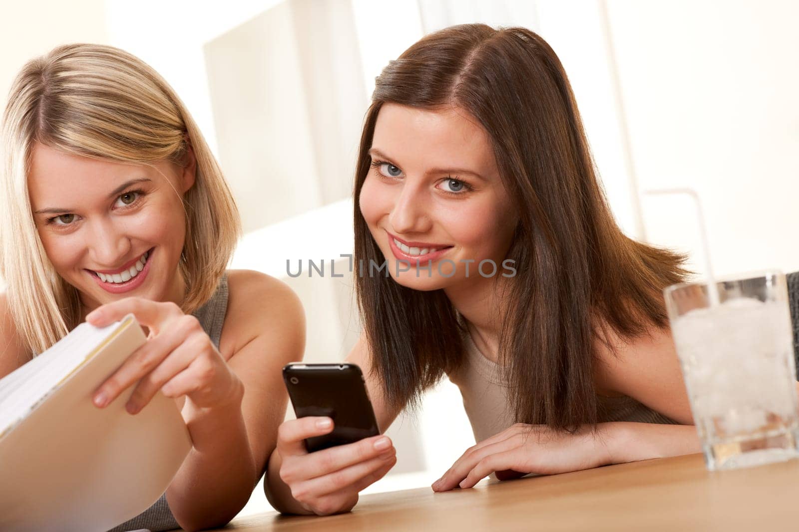 Two smiling students enjoying free time with book and mobile phone