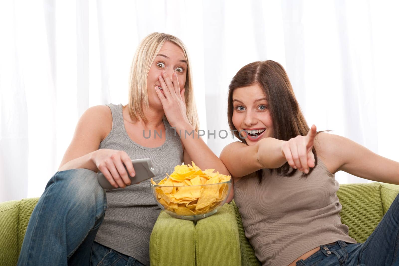 Two teenage girl watching television and eating potato chips