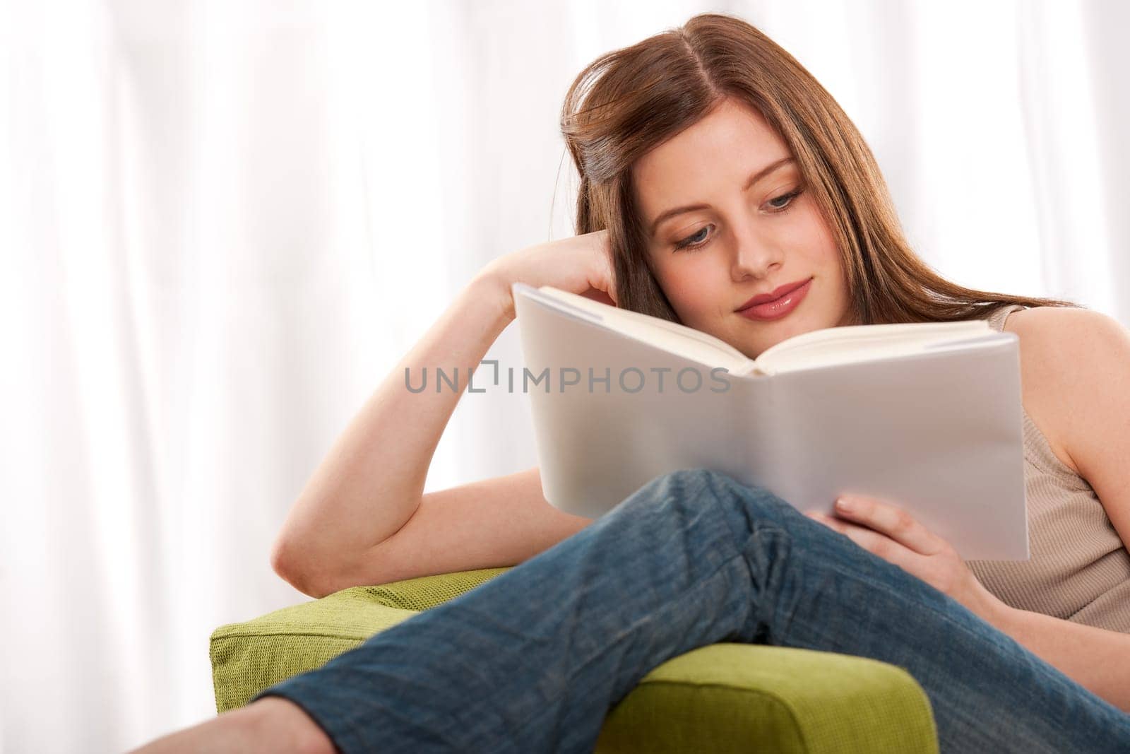 Young brunette reading book, sitting on green armchair