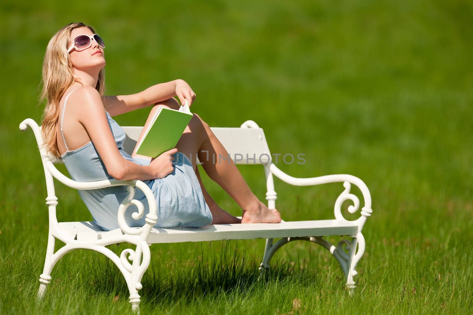 Spring and summer - Young woman relaxing in meadow on white bench on sunny day enjoying sun