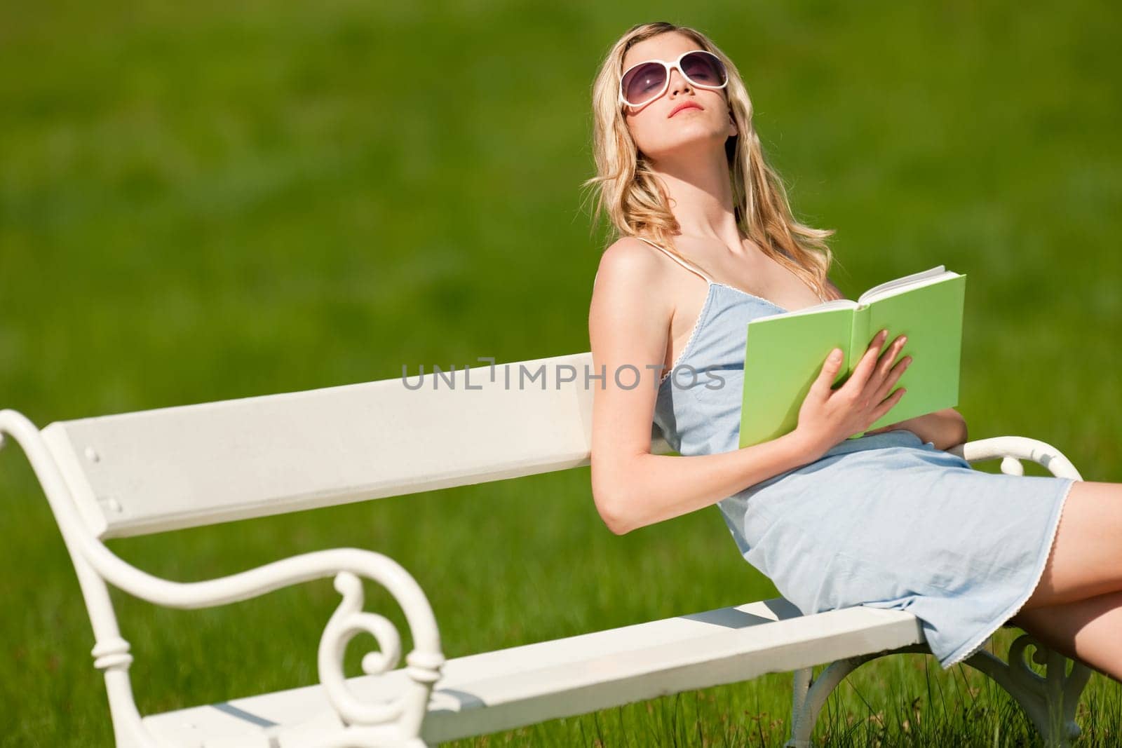 Spring and summer - Young woman relaxing in meadow on white bench on sunny day enjoying sun