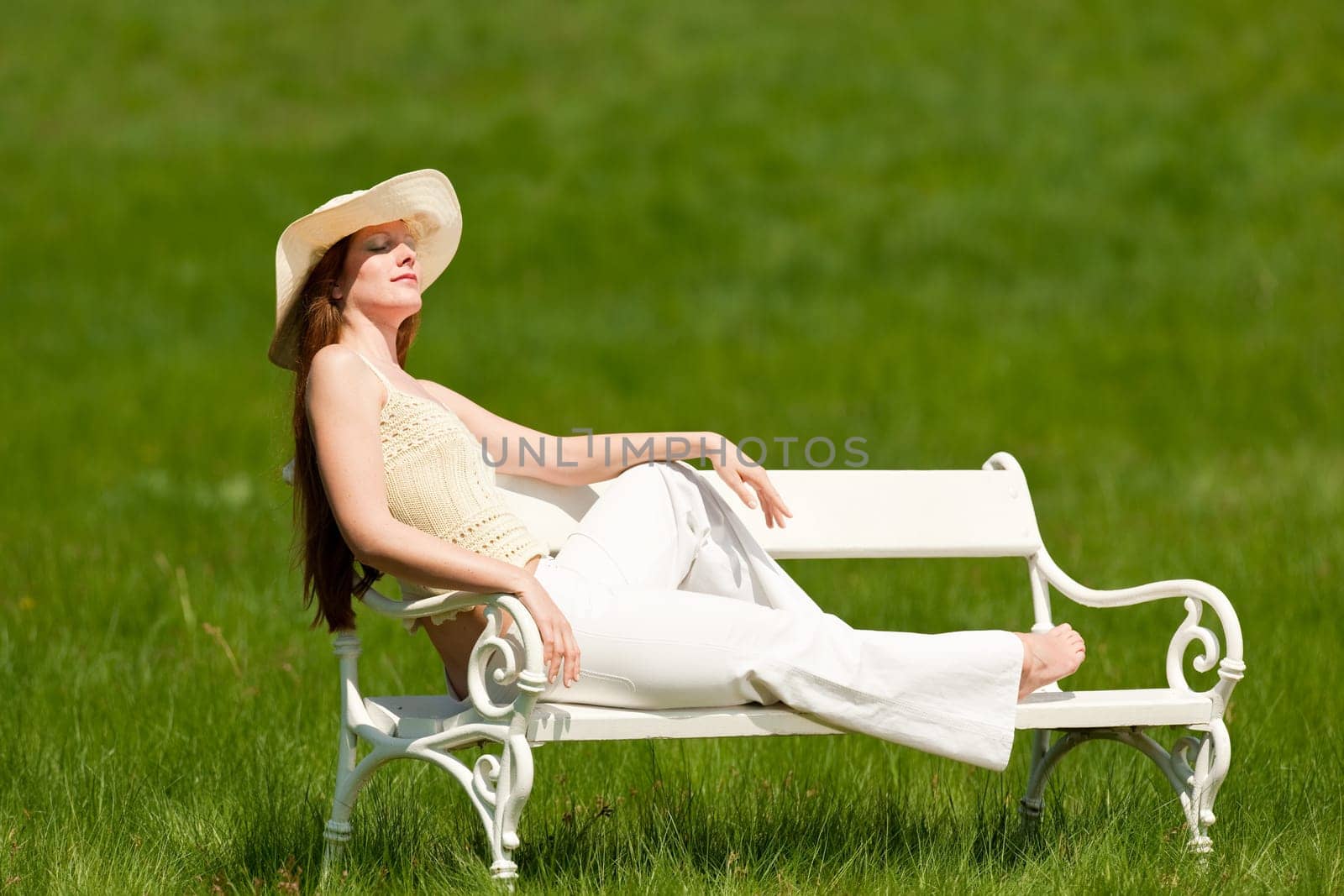 Red hair woman sitting on white bench in a meadow shallow DOF