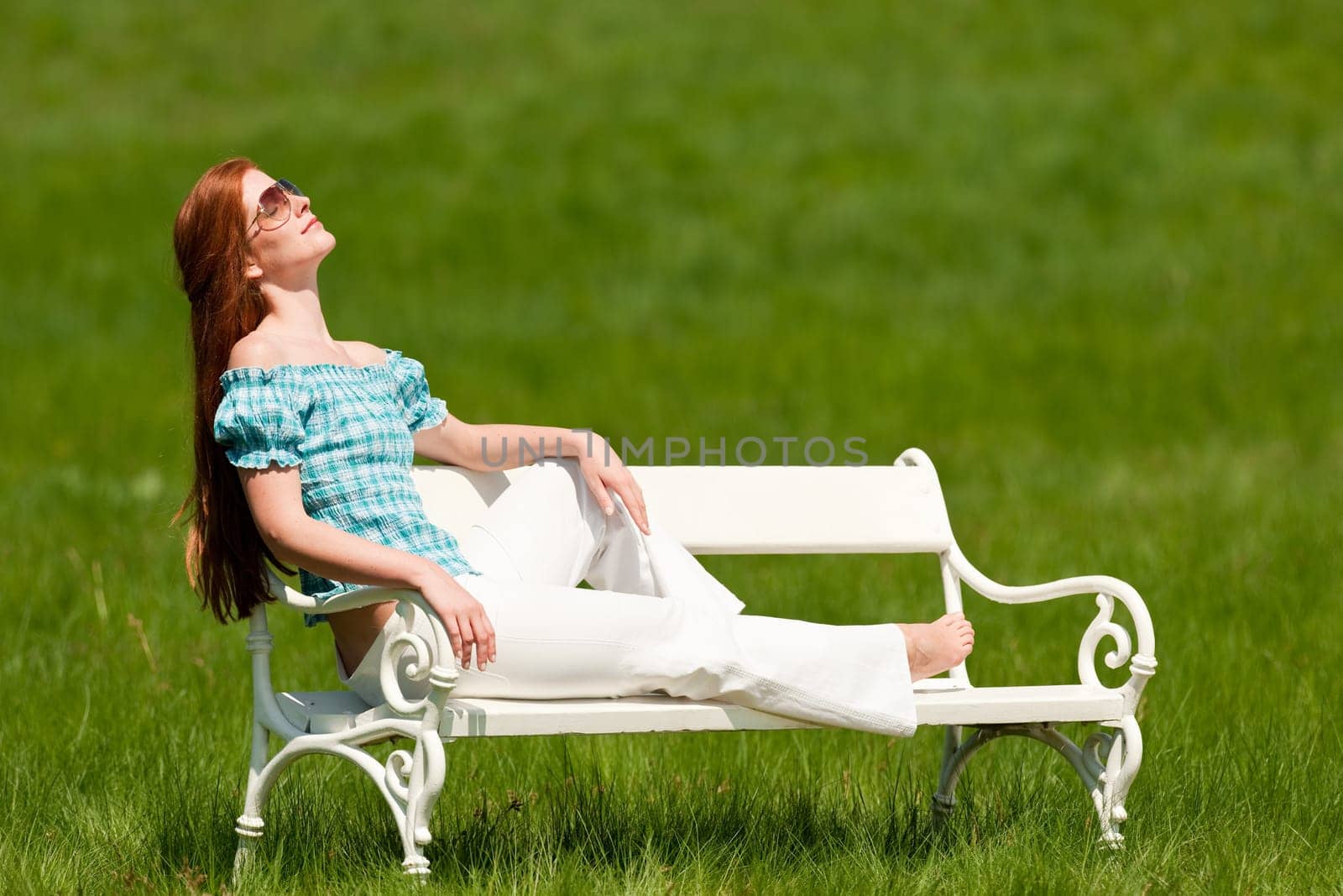 Red hair woman enjoying sun on white bench in a meadow shallow DOF