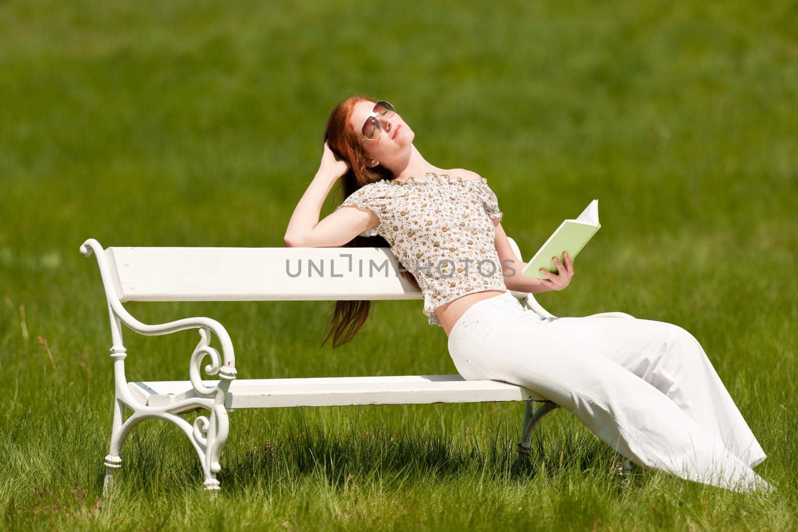 Red hair woman reading book on white bench in a meadow shallow DOF