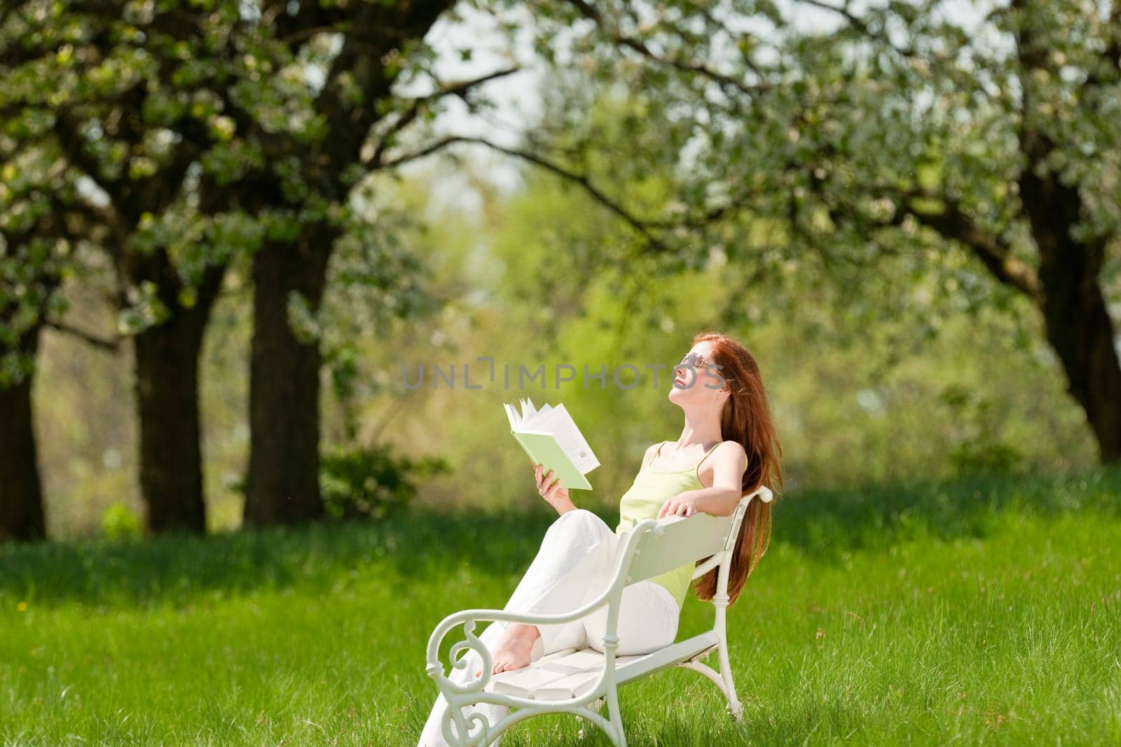 Red hair woman relaxing on white bench in a meadow shallow DOF