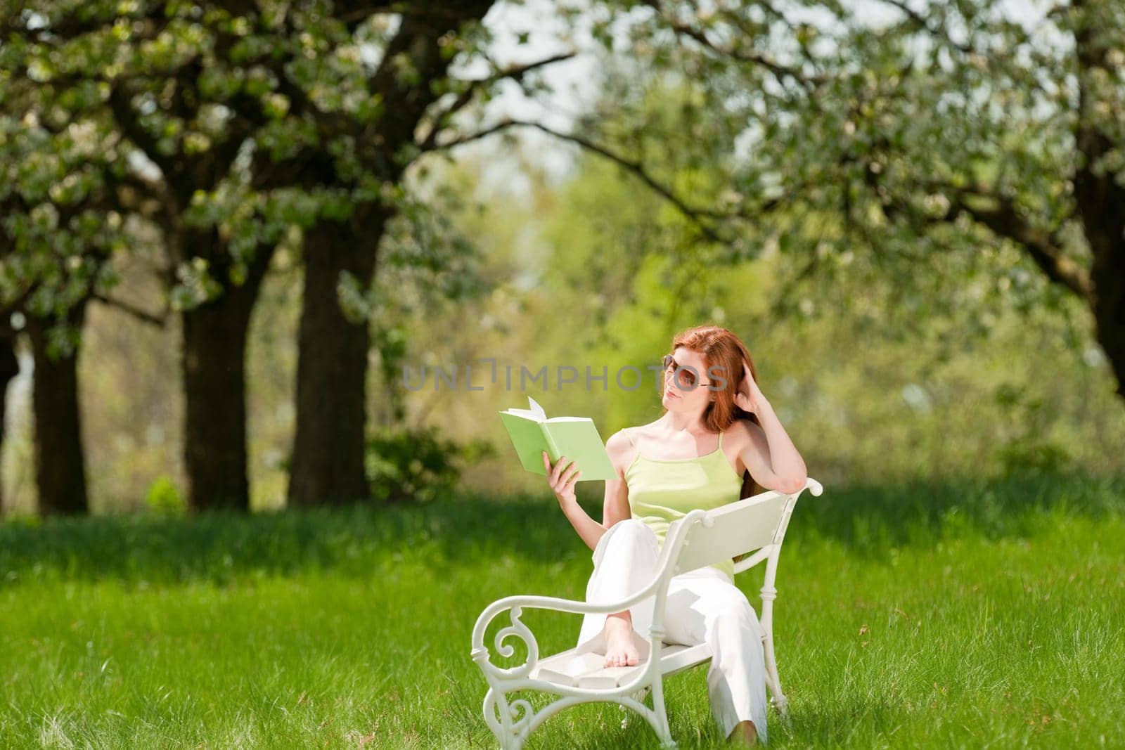 Red hair woman reading book on white bench in a meadow shallow DOF