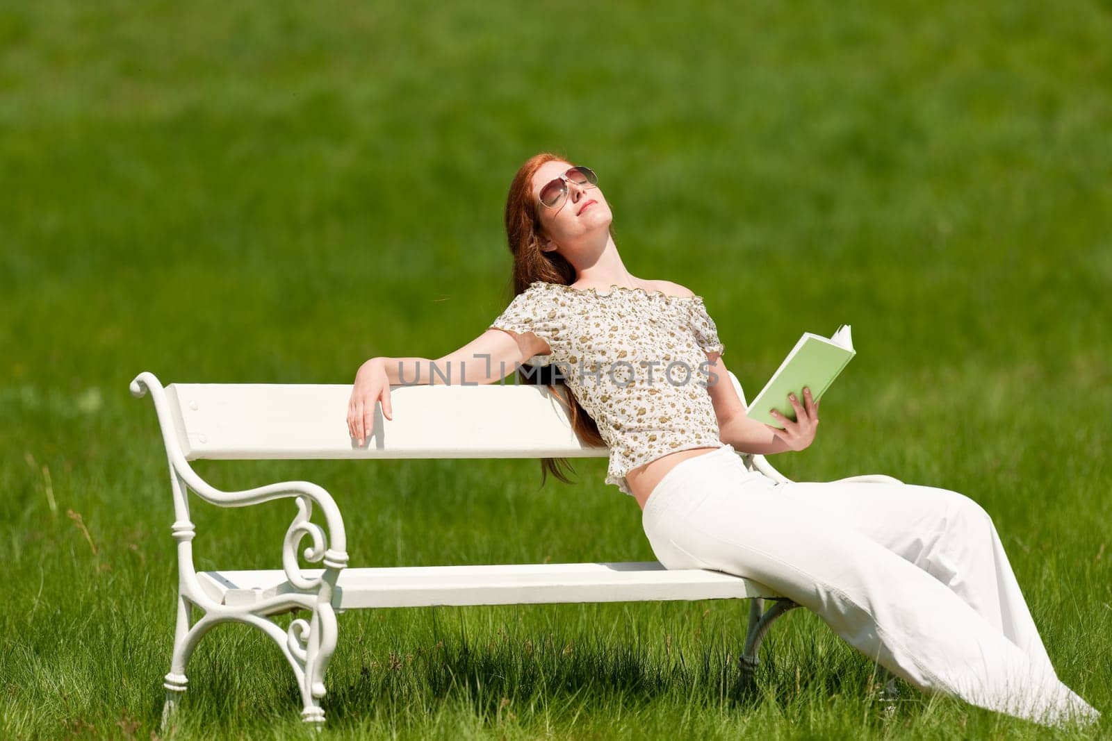 Red hair woman enjoying sun on white bench in a meadow shallow DOF