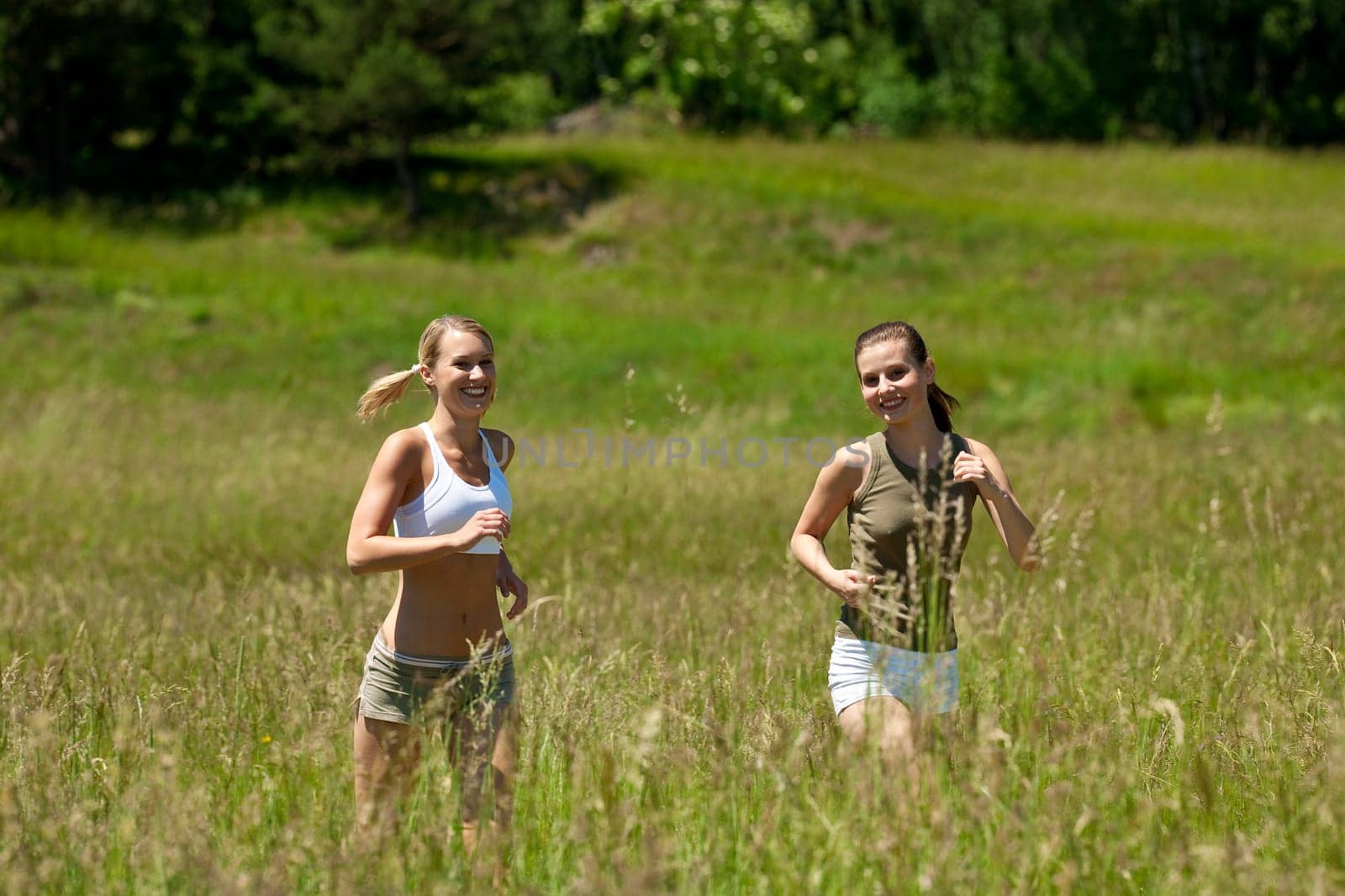 Two young woman jogging in a meadow on sunny day