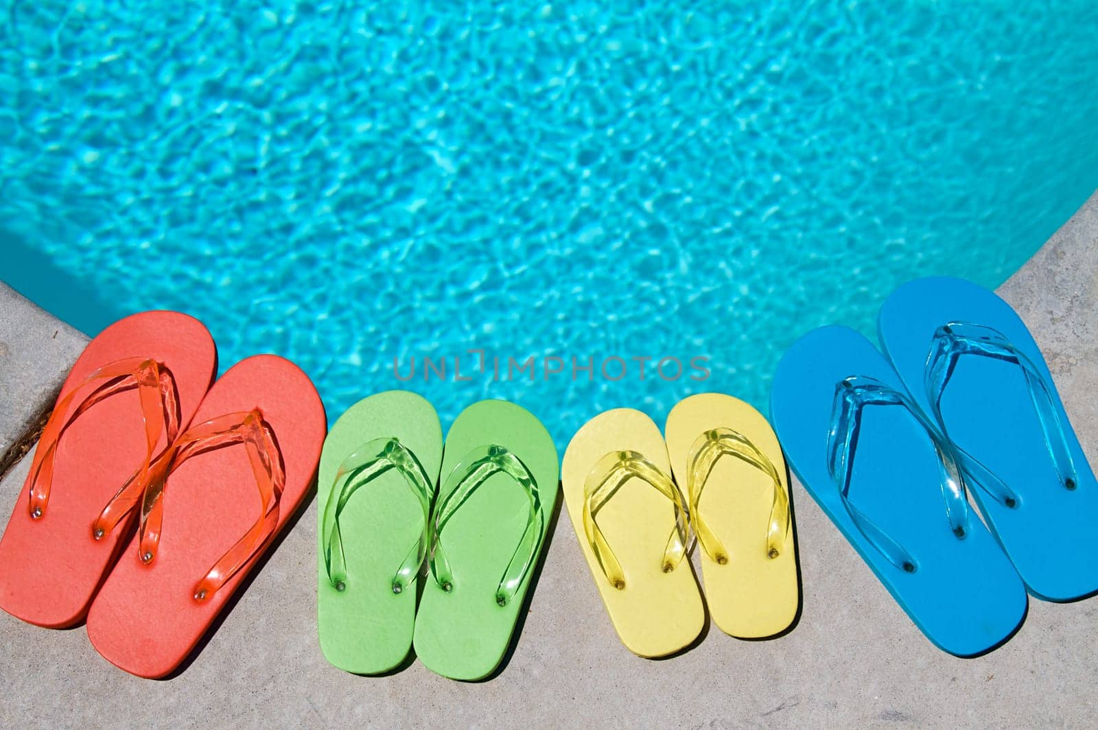 Colored flipflops of a family of four by the swimming pool