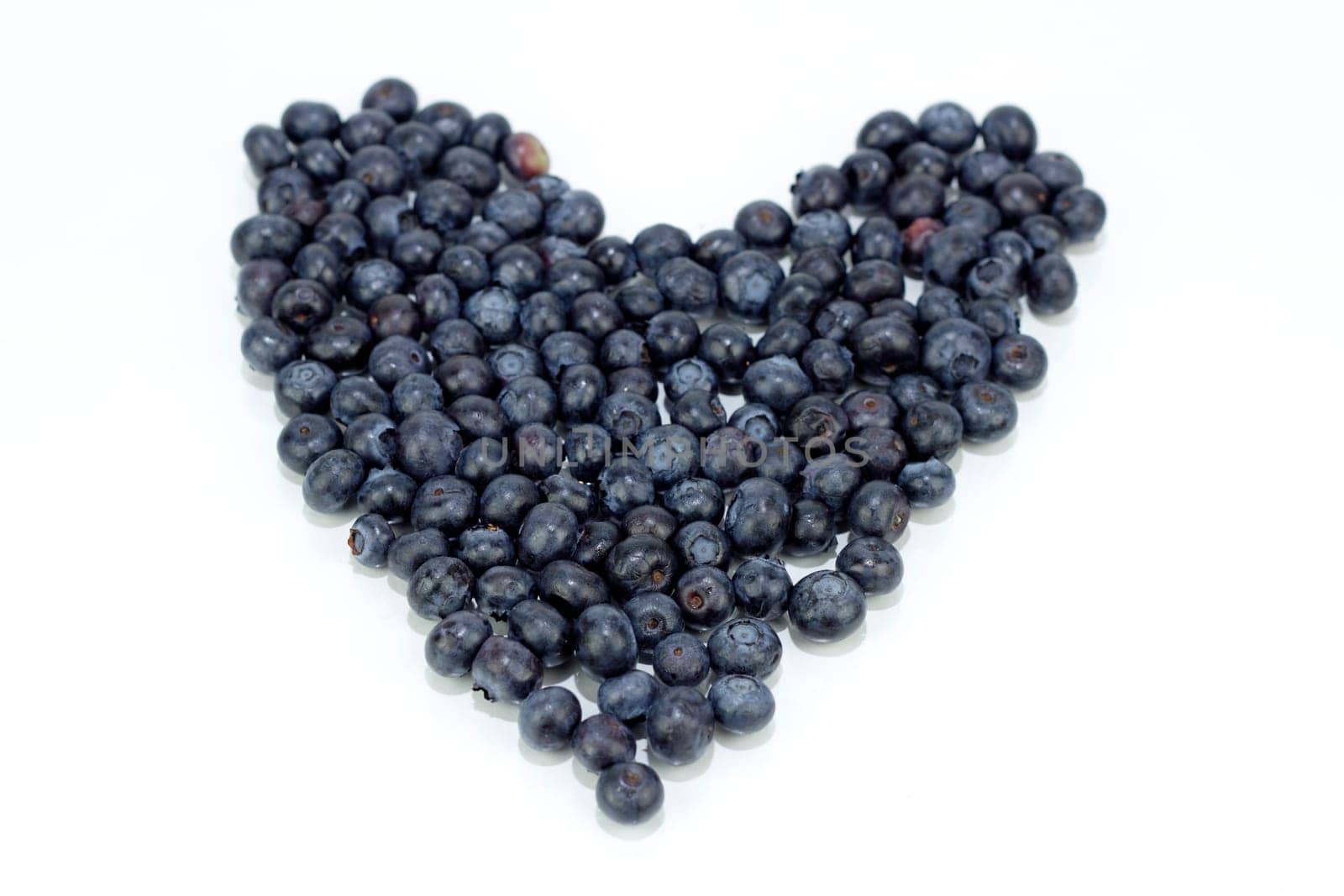 Blue purple fruit berry in the shape of love on a reflective white background.