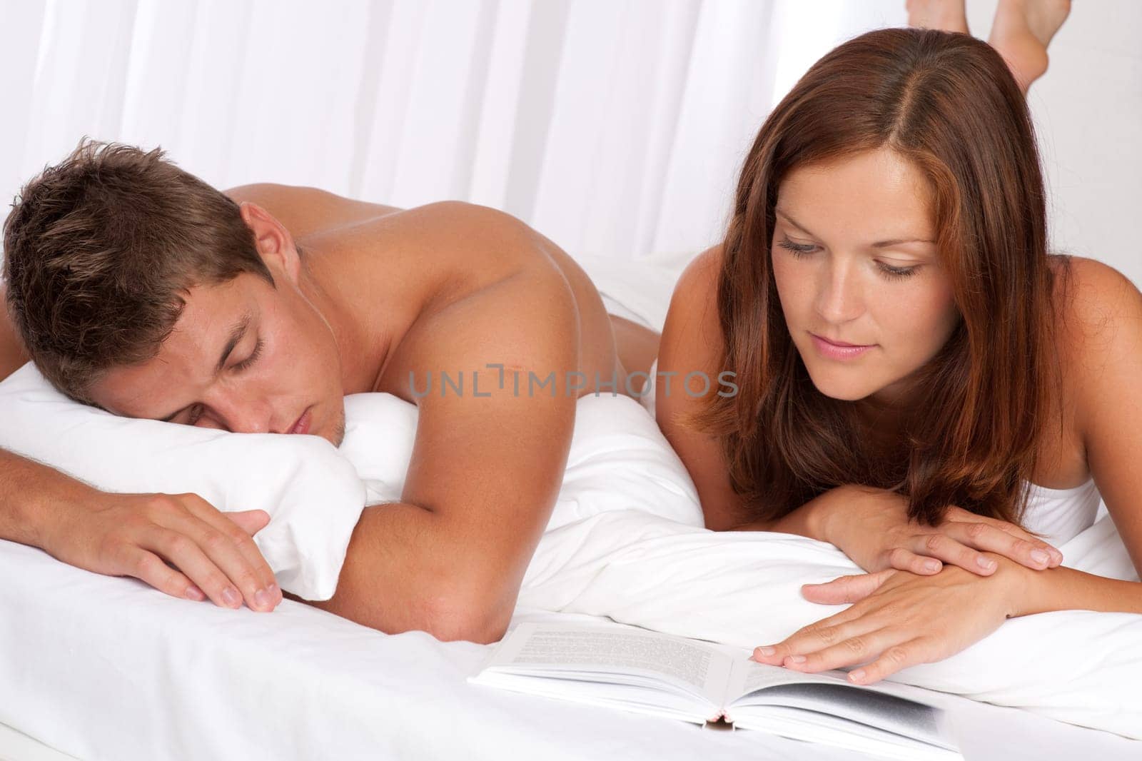 Young man and woman lying down on white sofa, woman reading book