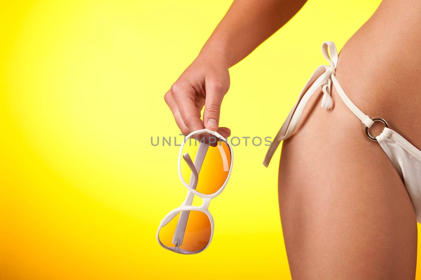 Part of female body with white bikini and sunglasses on yellow background