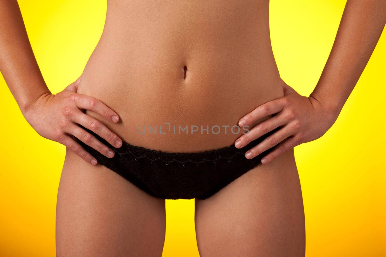 Part of female body wearing black bikini on yellow background