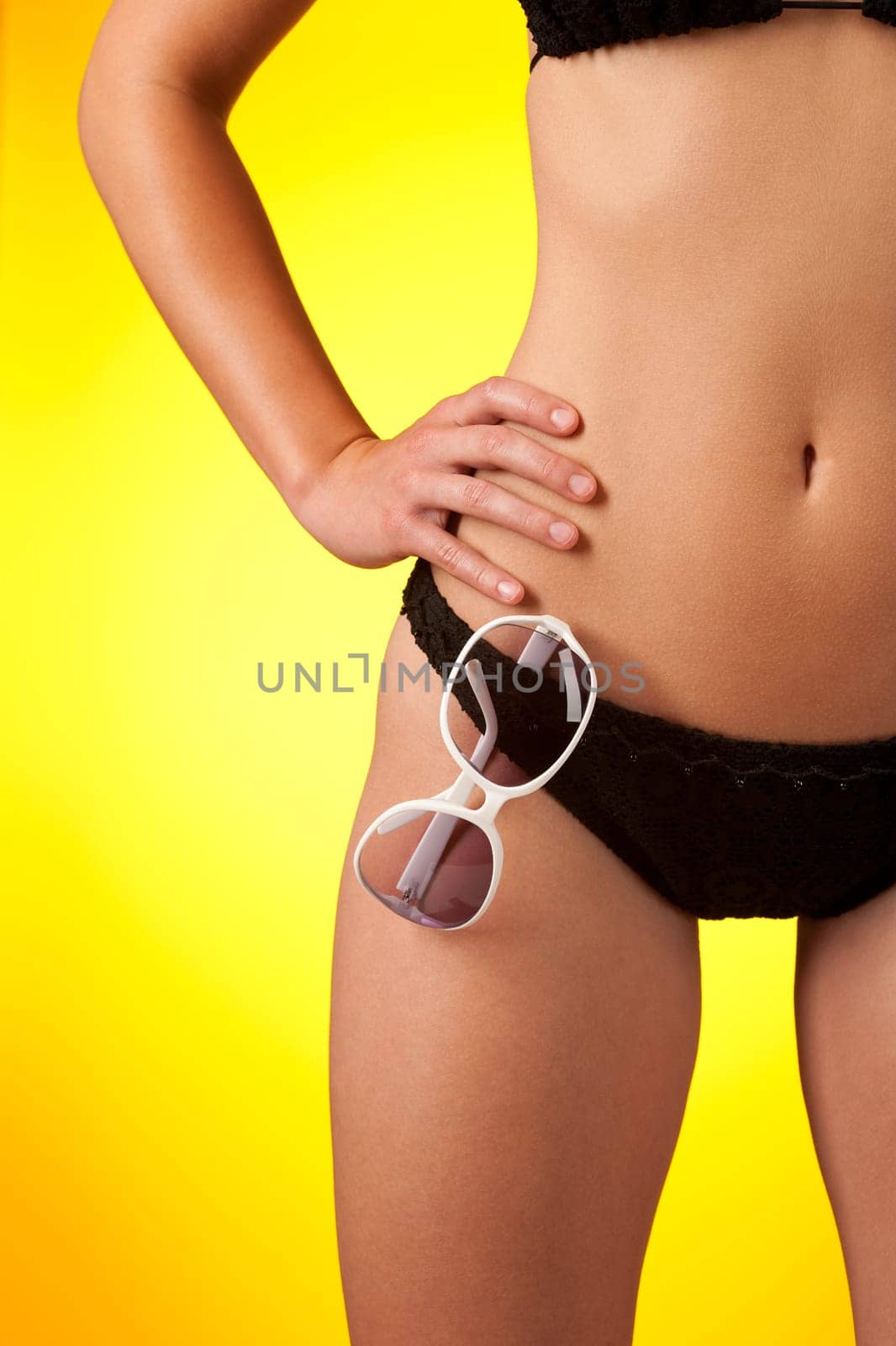 Part of female body wearing black bikini and sunglasses on yellow background