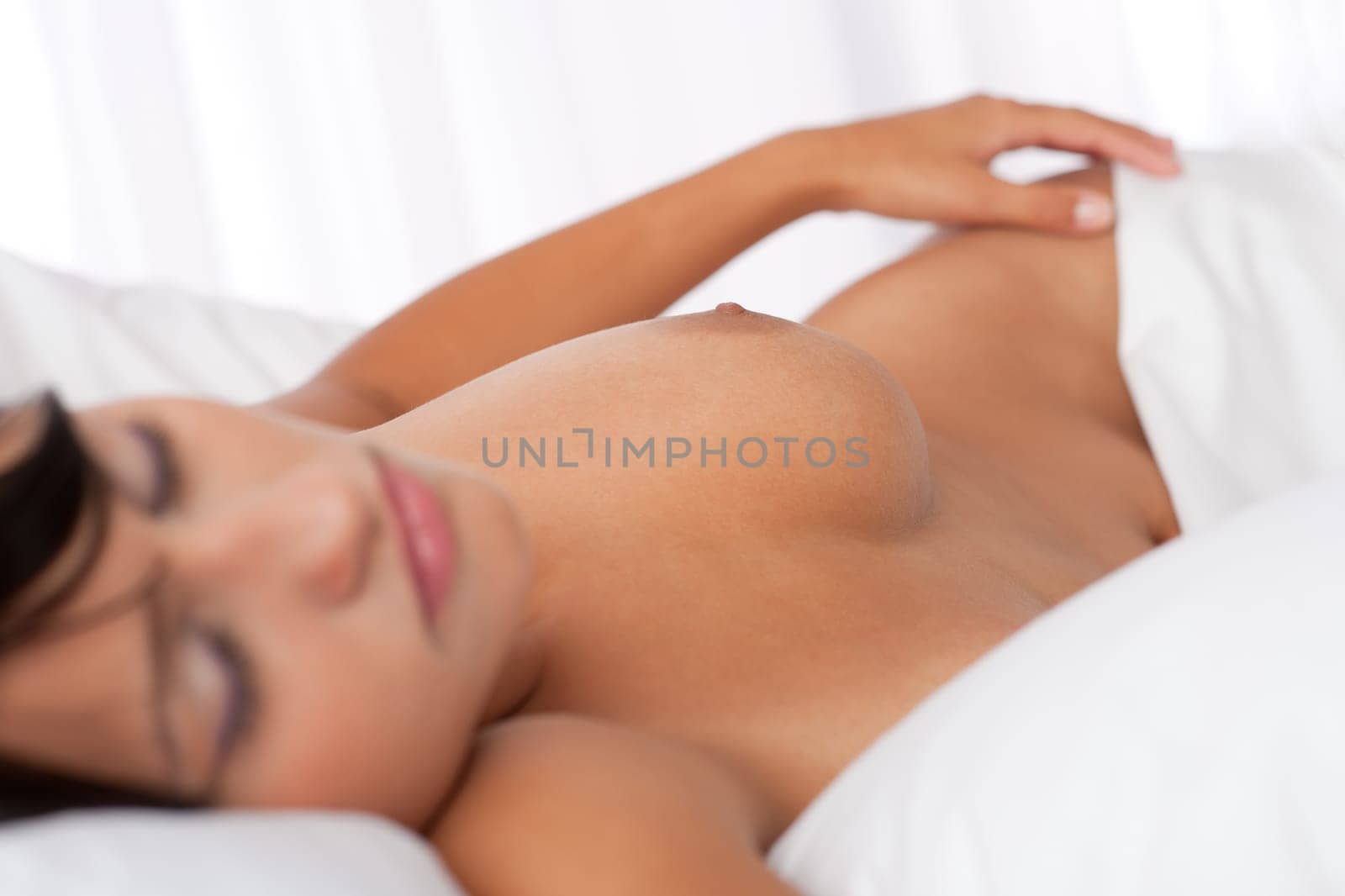 Brown hair woman sleeping naked in white bed, focus on nipple, shallow DOF