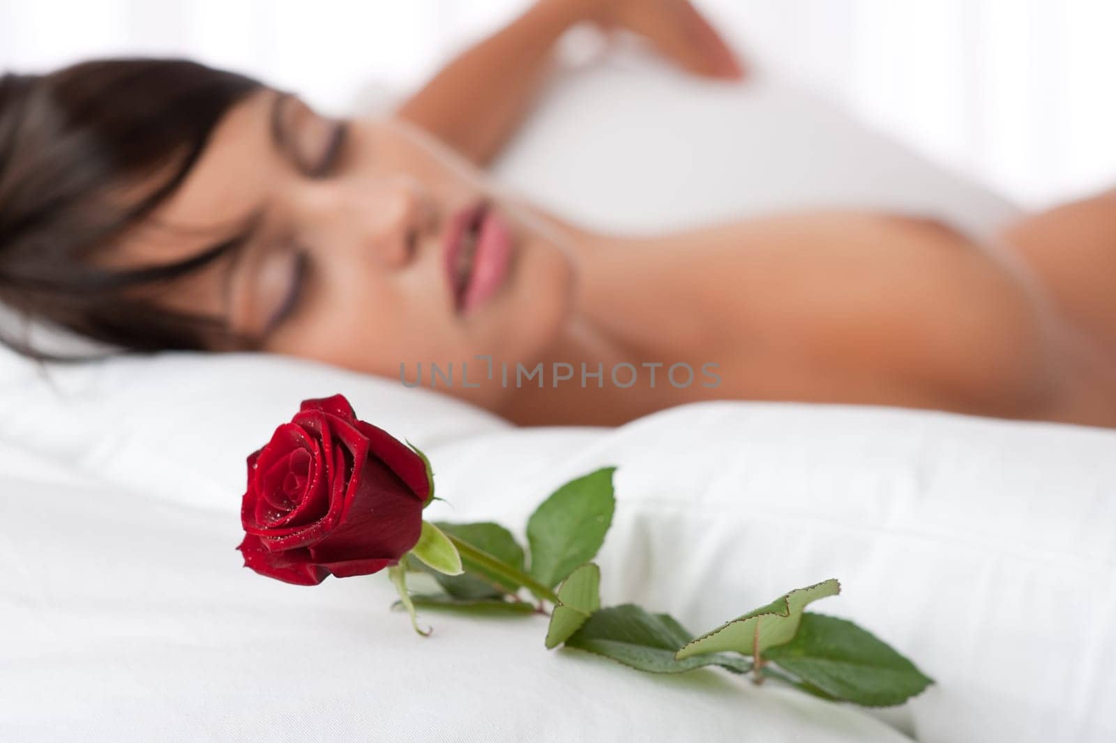 Woman lying in white bed, focus on rose, shallow DOF